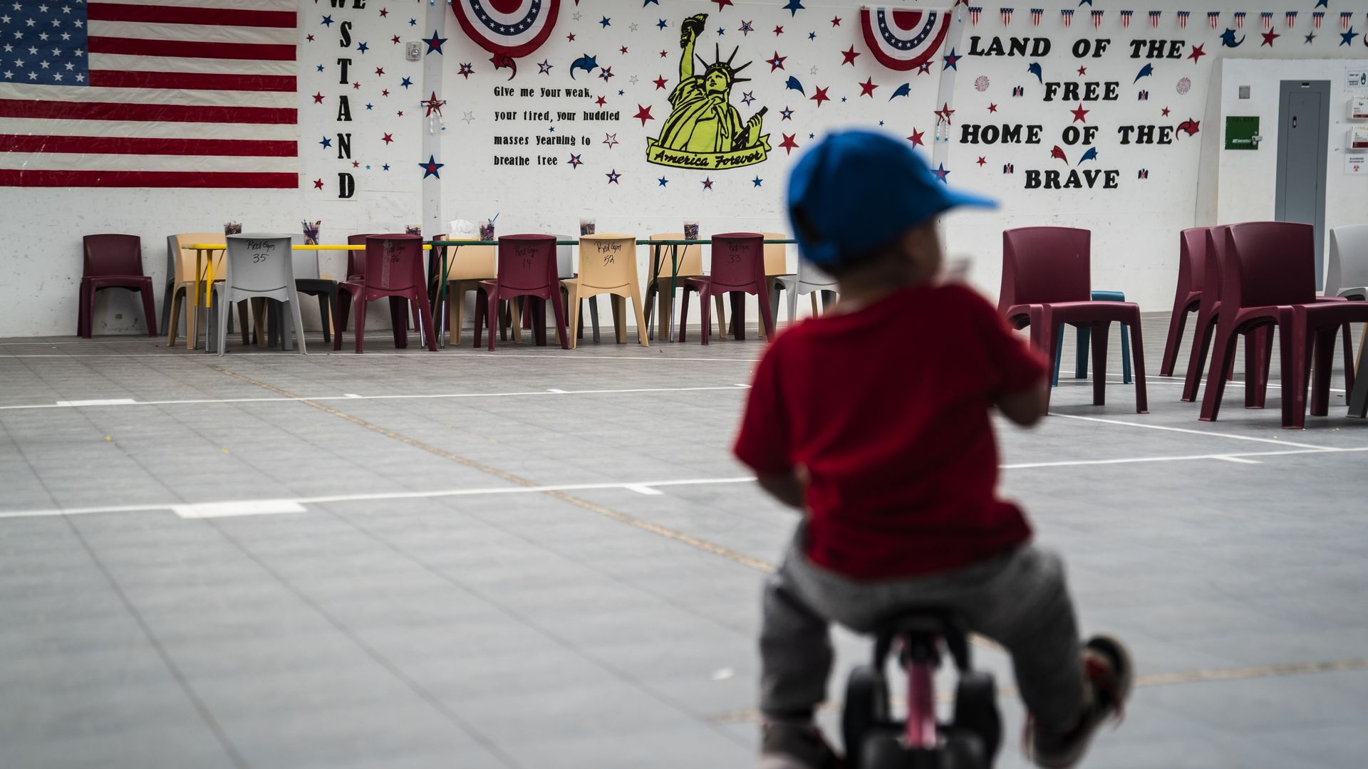 An immigrant child plays in front of patriotic phrases and symbols covering the walls in a gymnasium at U.S. Immigration and Customs Enforcement's South Texas Family Residential Center