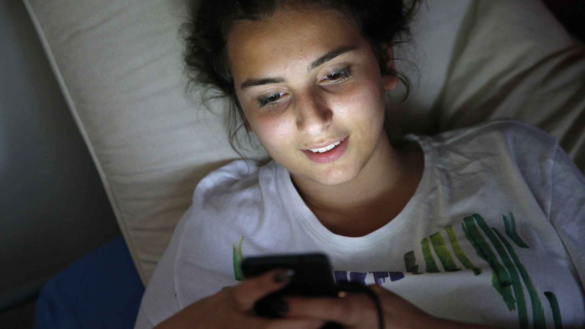 Teenager using a cell phone on her bed.