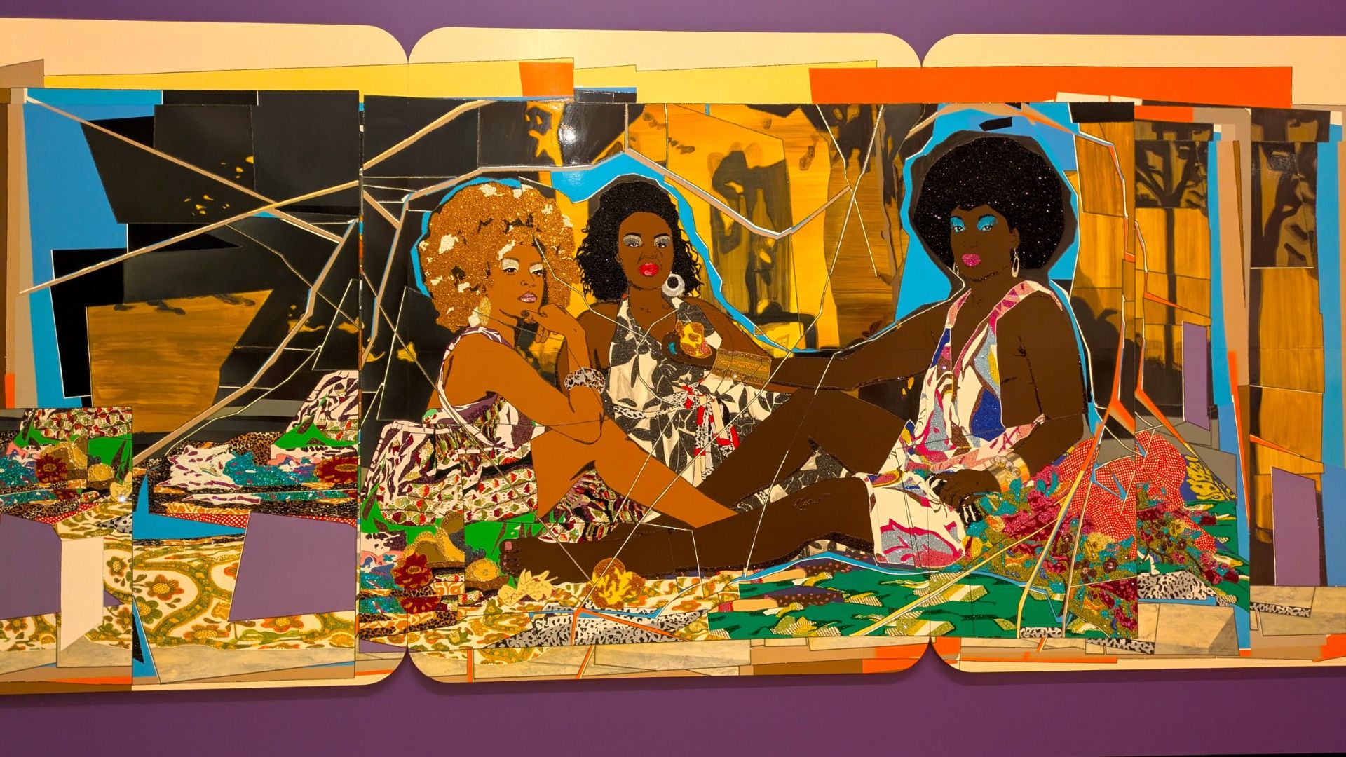 Colorful collage mural of three Black women lounging together, rendered in fractured, geometric shapes. Bright blues, yellows, and oranges with patterned fabrics and bold hairdos.