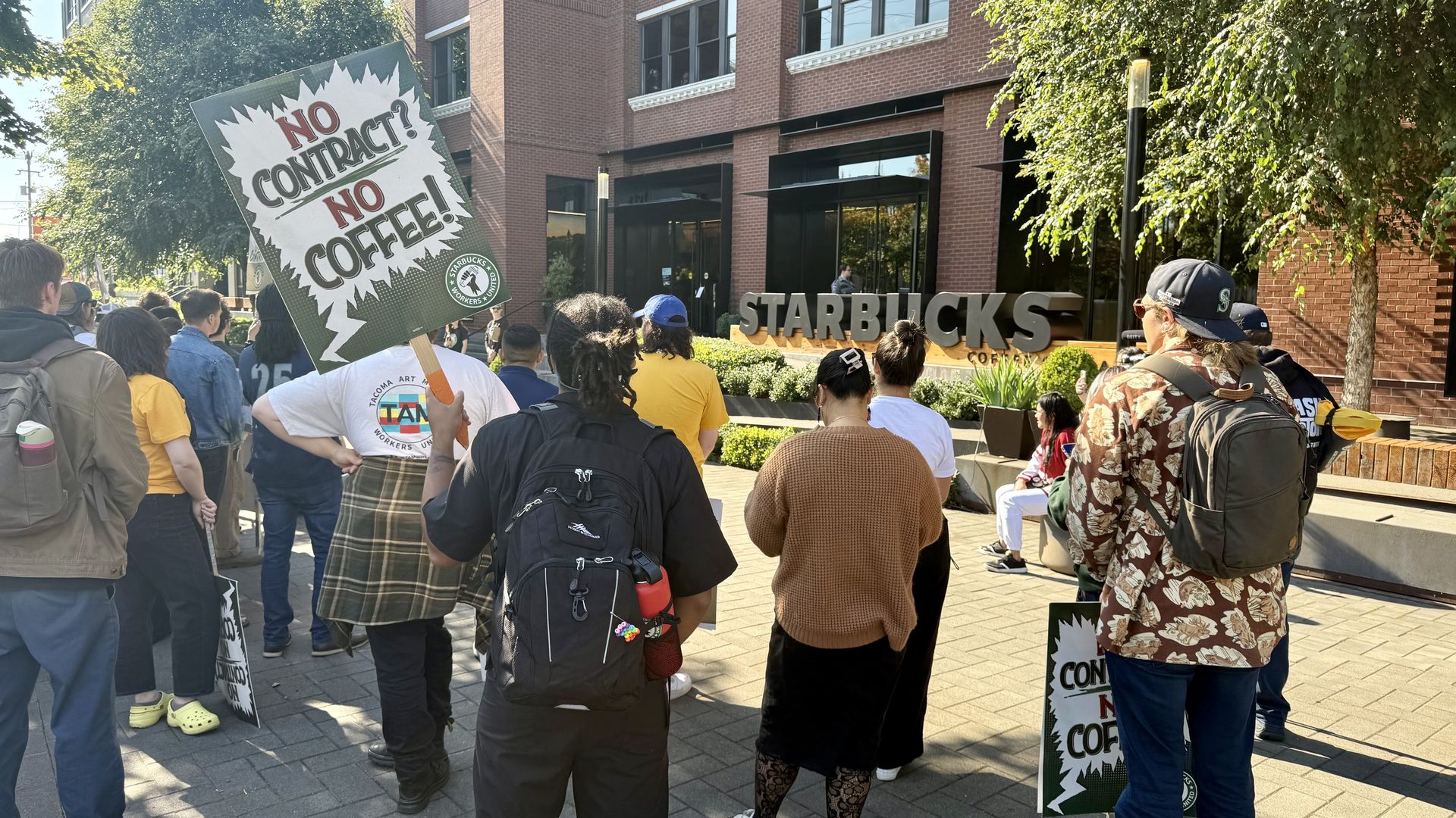 People with signs rally outside a brick building. 