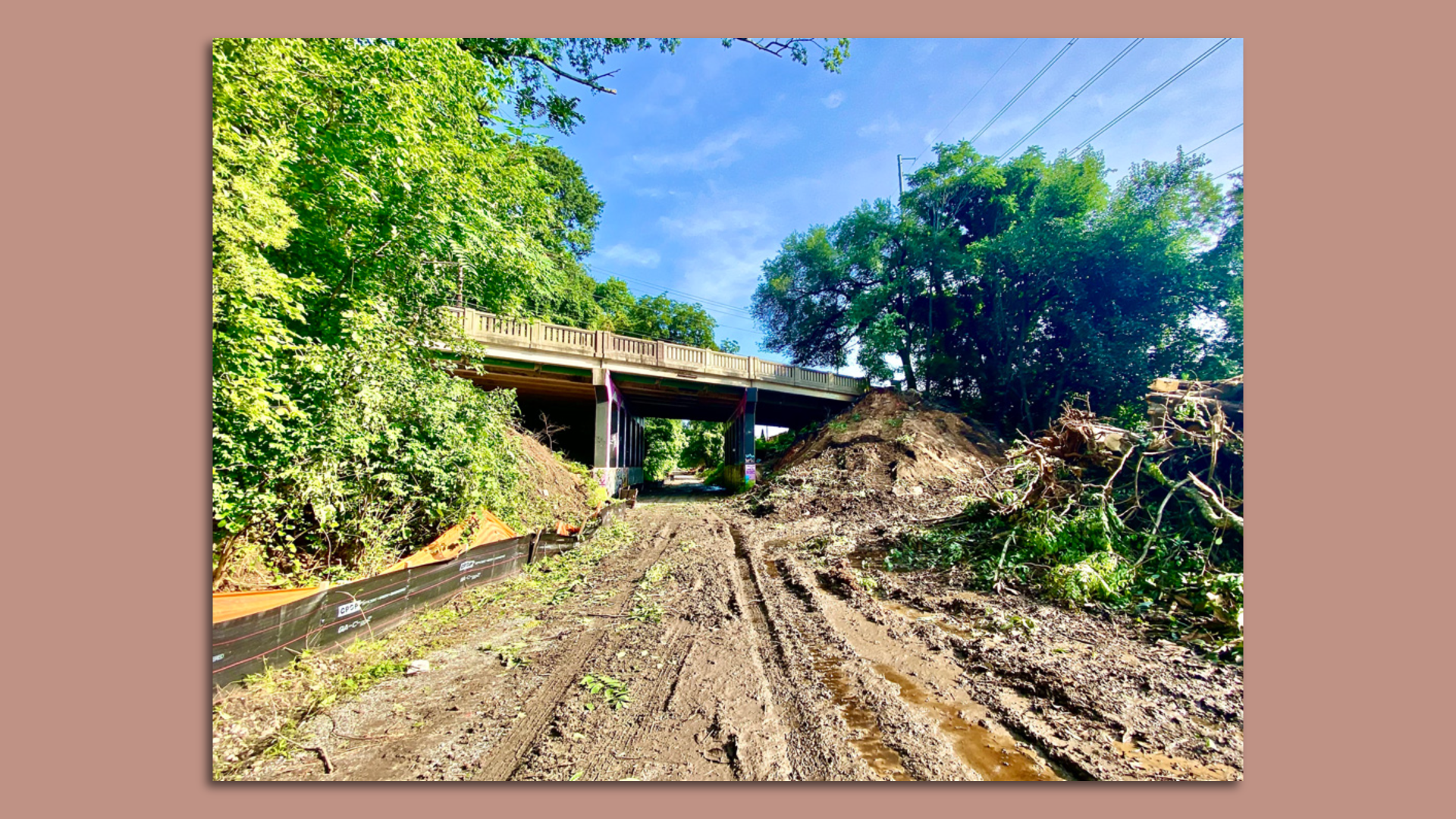 A photo of a muddy dirt trail running underneath a bridge and which is being turned into a bike lane