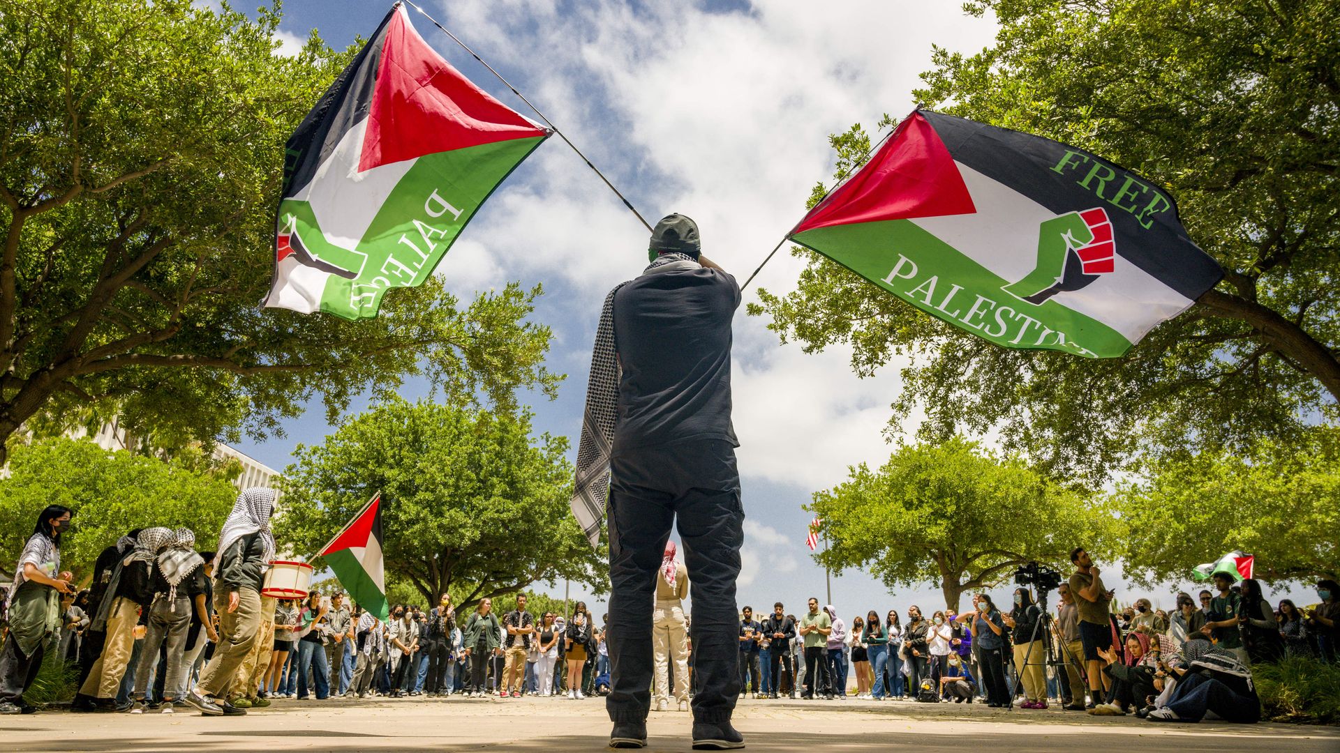 A man waves two Palestinian flags while other demonstrators look on.