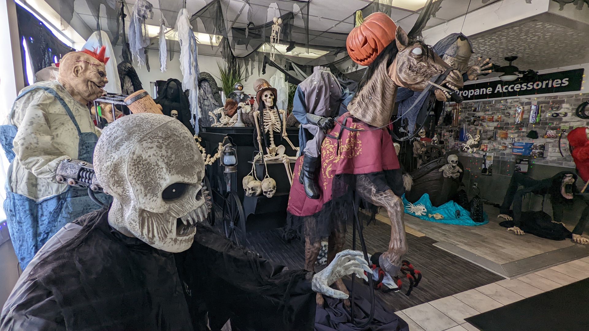 Elaborate Halloween decorations appear next to a storefront wall with a sign that says "Propane Accessories" 