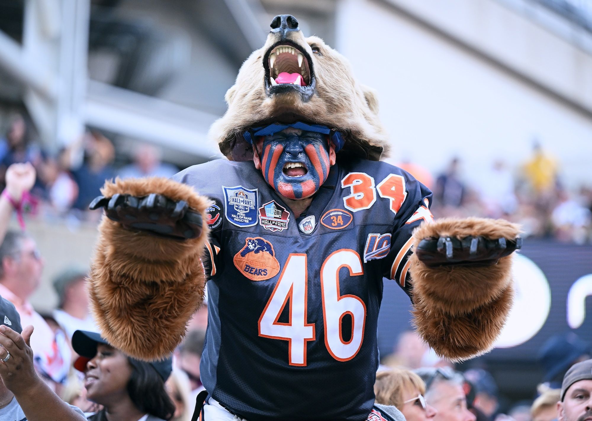 A man dressed in a bear costume, wearing a Bears jersey with orange and blue paint on his face.