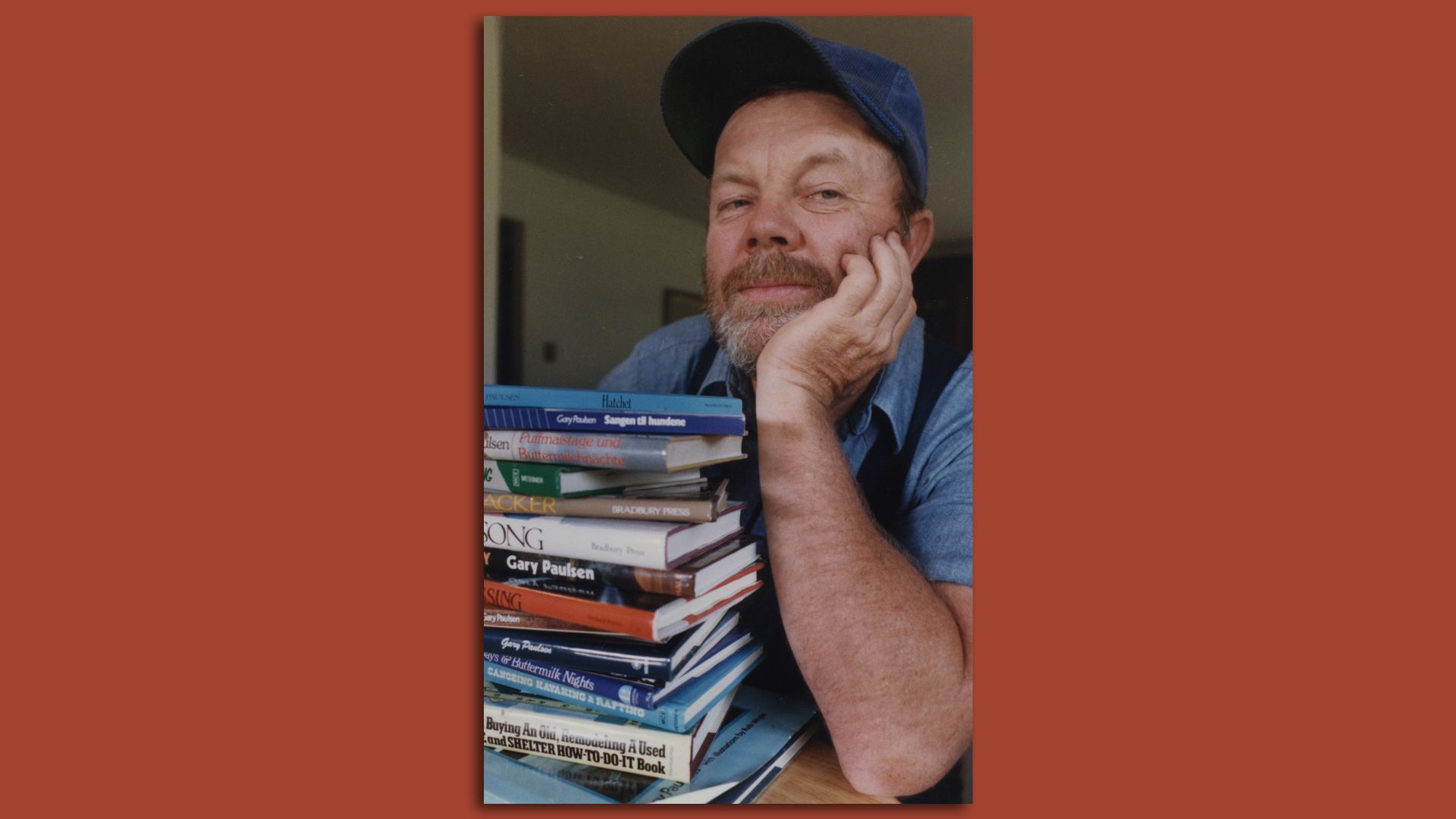 Gary Paulsen sits with his arm on his chin behind a stack of his books 