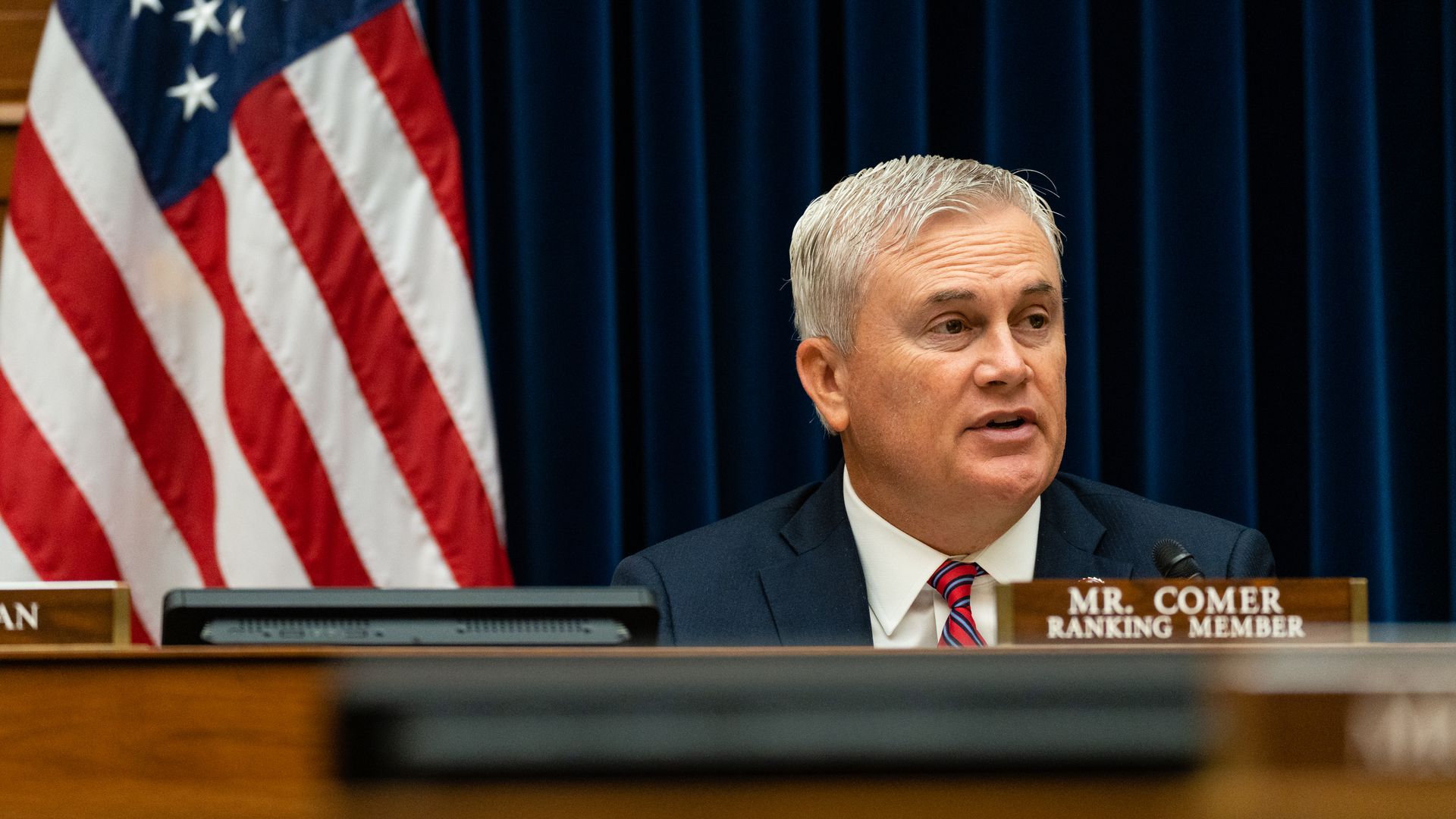 Rep. James Comer, wearing a blue suit and red tie, sits behind the dais and a placard with his name and title at a House Oversight Committee hearing.