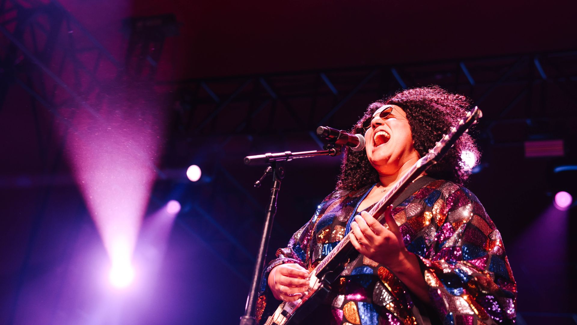 An image of Brittany Howard singing on a microphone with a purple light in the background.