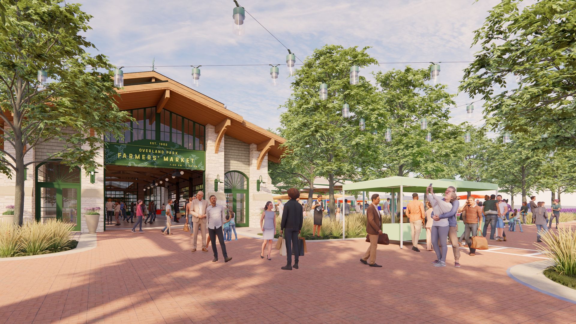 Outdoor farmers market plaza with brick-paved walkway, green-framed entrance reading Overland Park Farmers Market, string lights above, lush trees, and groups of people browsing stalls on sunny day.