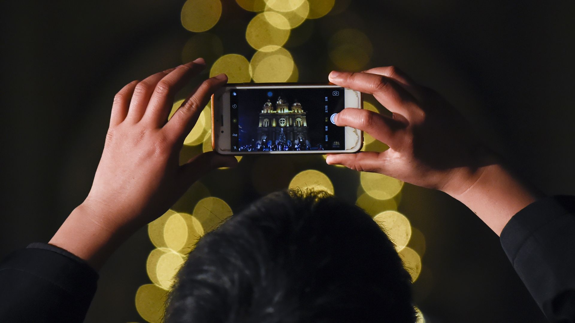 Man uses cell phone to take picture of Christmas lights, which are out of focus