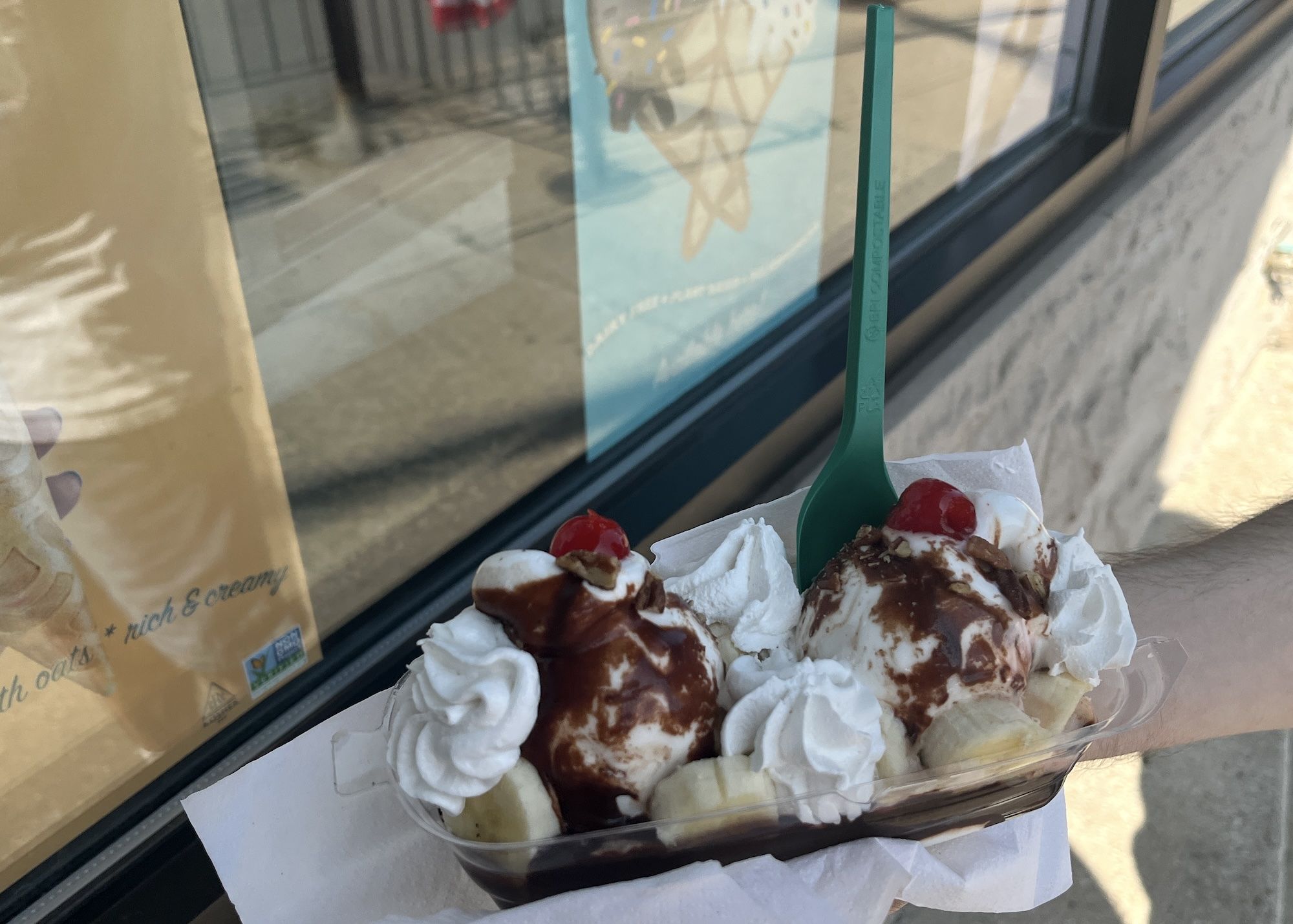 Banana split with whipped cream and chocolate sauce with a green plastic spoon.