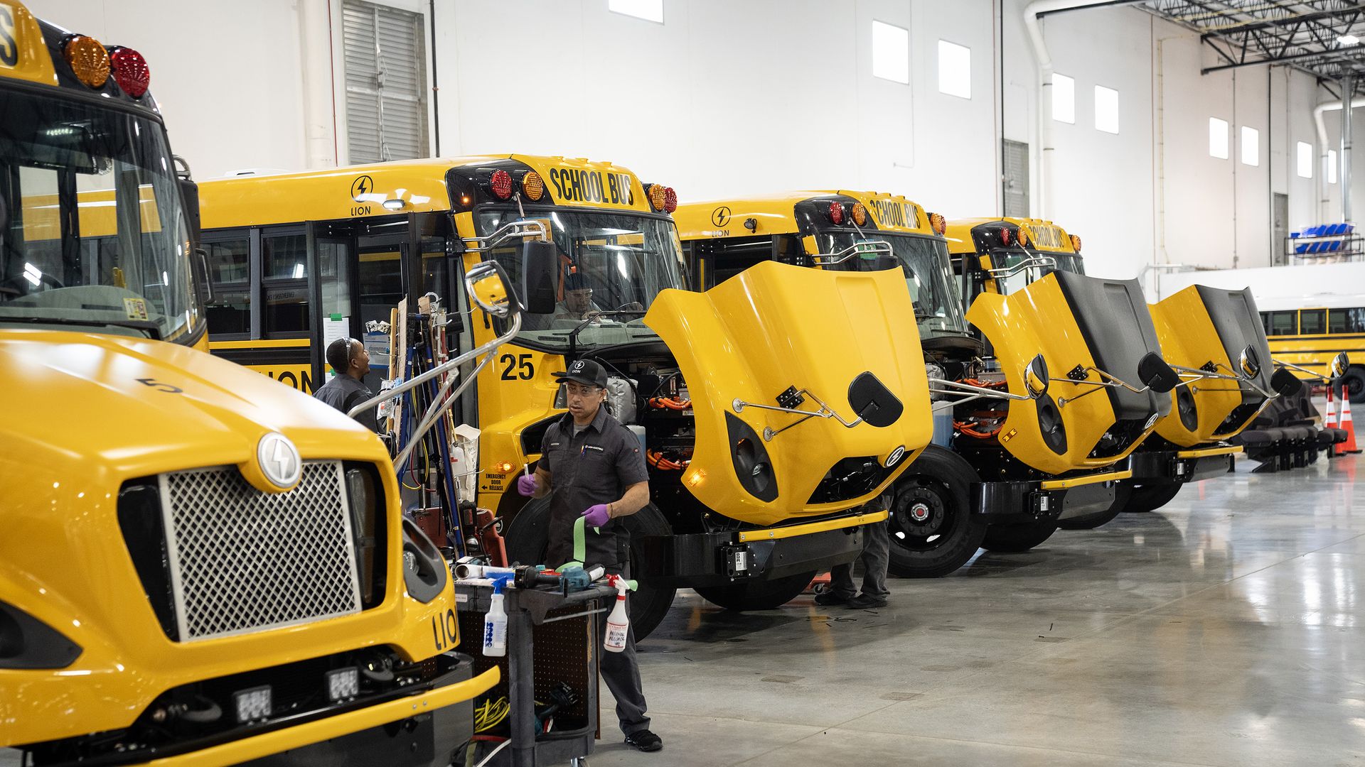 Workers inspect and repair electric yellow school buses with open hoods inside Lion Electric's Illinois factory, which has since closed. 