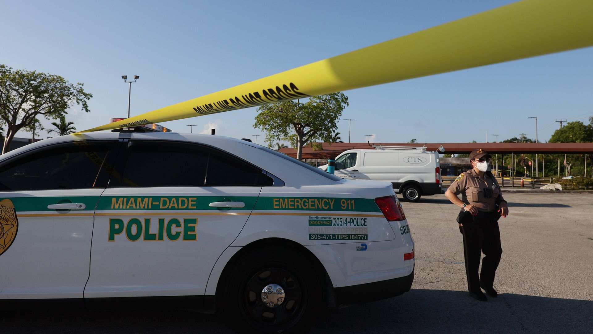 A white Miami-Dade police vehicle is parked next to yellow crime scene tape. 