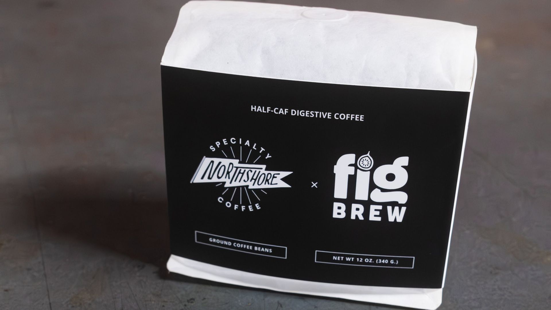 White bag of ground coffee beans with a black label reading "Northshore Specialty Coffee x fig Brew" and "Half-Caf Digestive Coffee" on a gray surface.