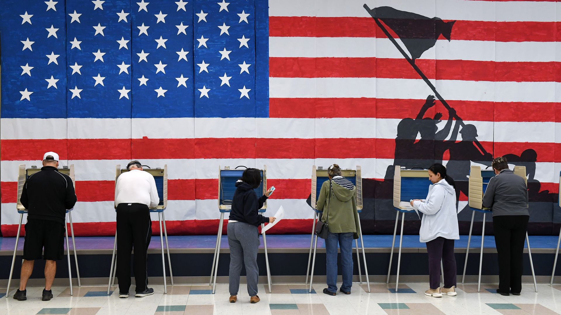 People voting at booths with an American flag background. 