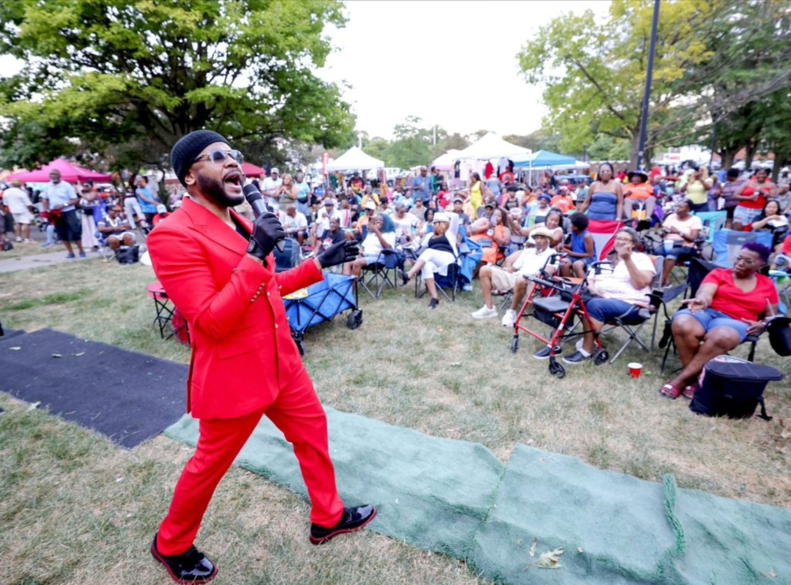 A singer in a red suit performs for a crowd in a park