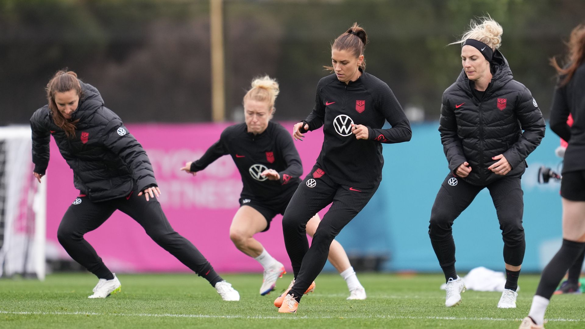 Four players on the women's national soccer team during a practice. They all wear black uniforms.