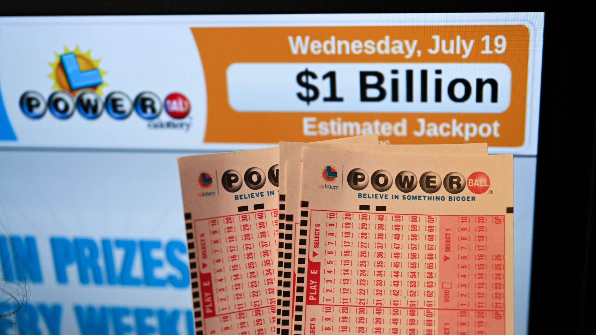 Powerball play slips in front of computer screen that says $1 billion estimated jackpot for Wednesday, July 19