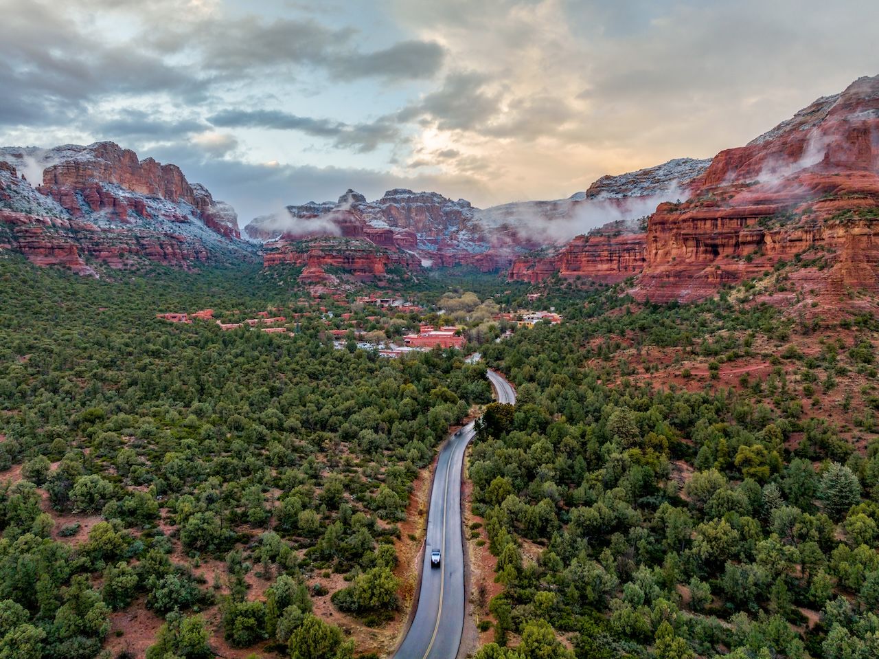 A photo of a red rock buttee valley with snow capped peaks and a main road cutting through.