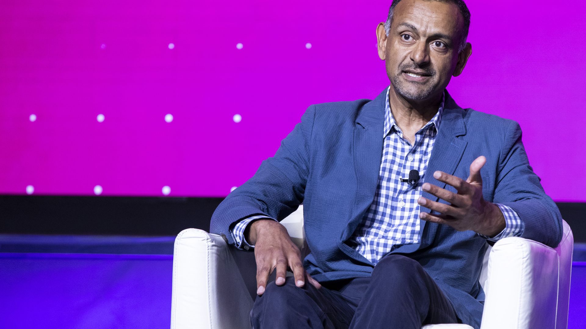 Coinbase's attorney speaking on stage at a conference in casual business attire, sitting in a chair. 