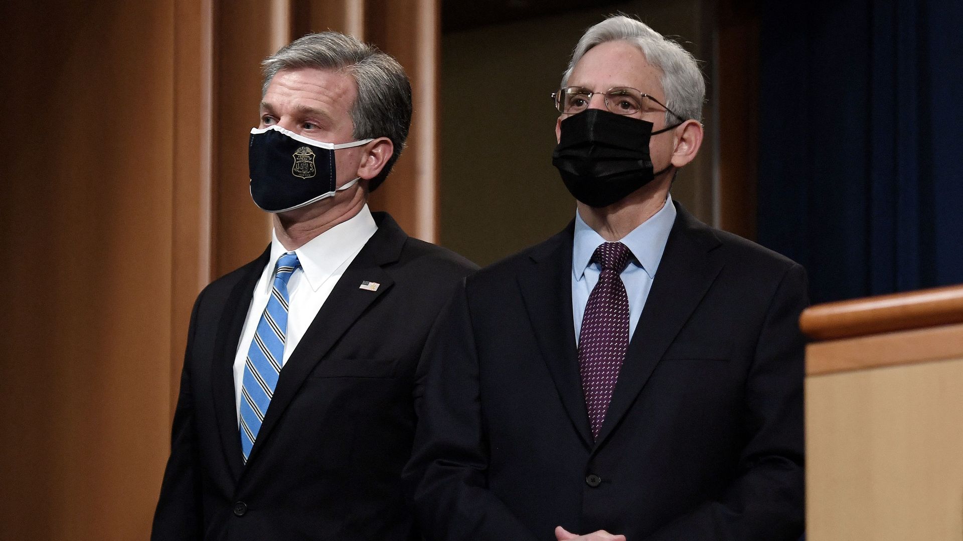 FBI Director Christopher Wray and Attorney General Merrick Garland standing next to each other, both wearing masks.