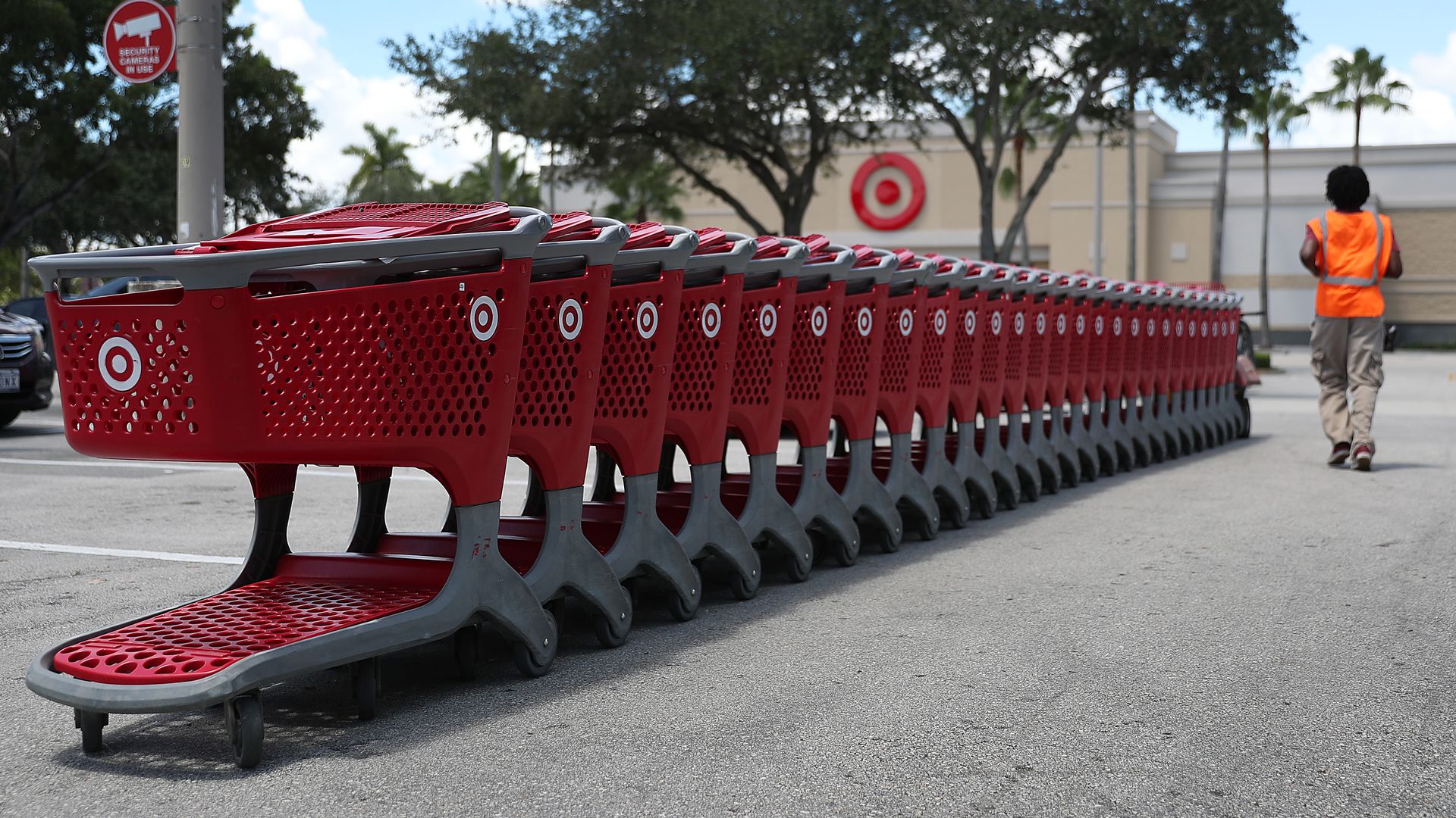 An employee in an orange vest walks by a row of red shopping carts