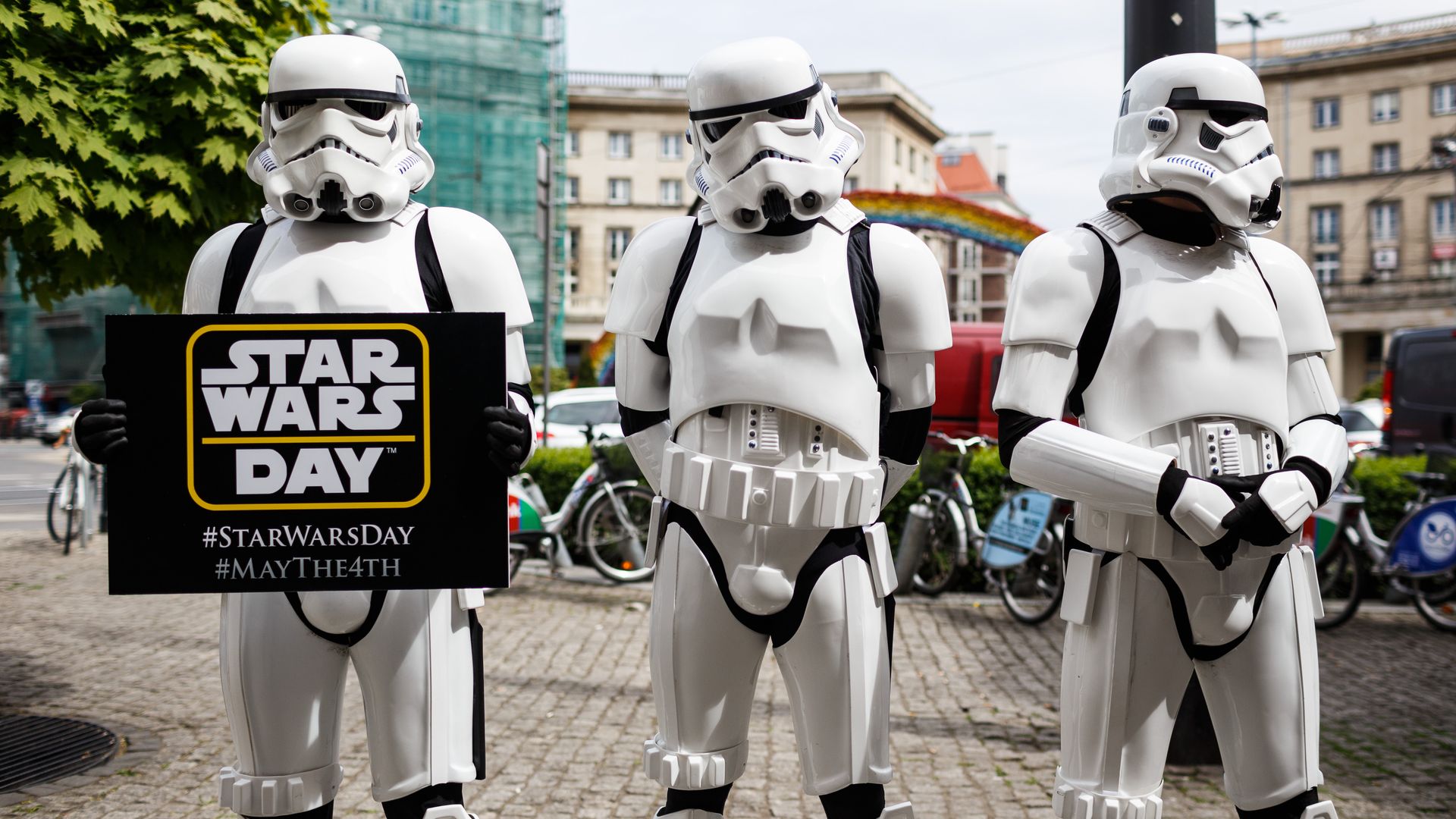 Three storm troopers from the Star Wars movies stand side by side. One is holding a sign that reads Star Wars Day.
