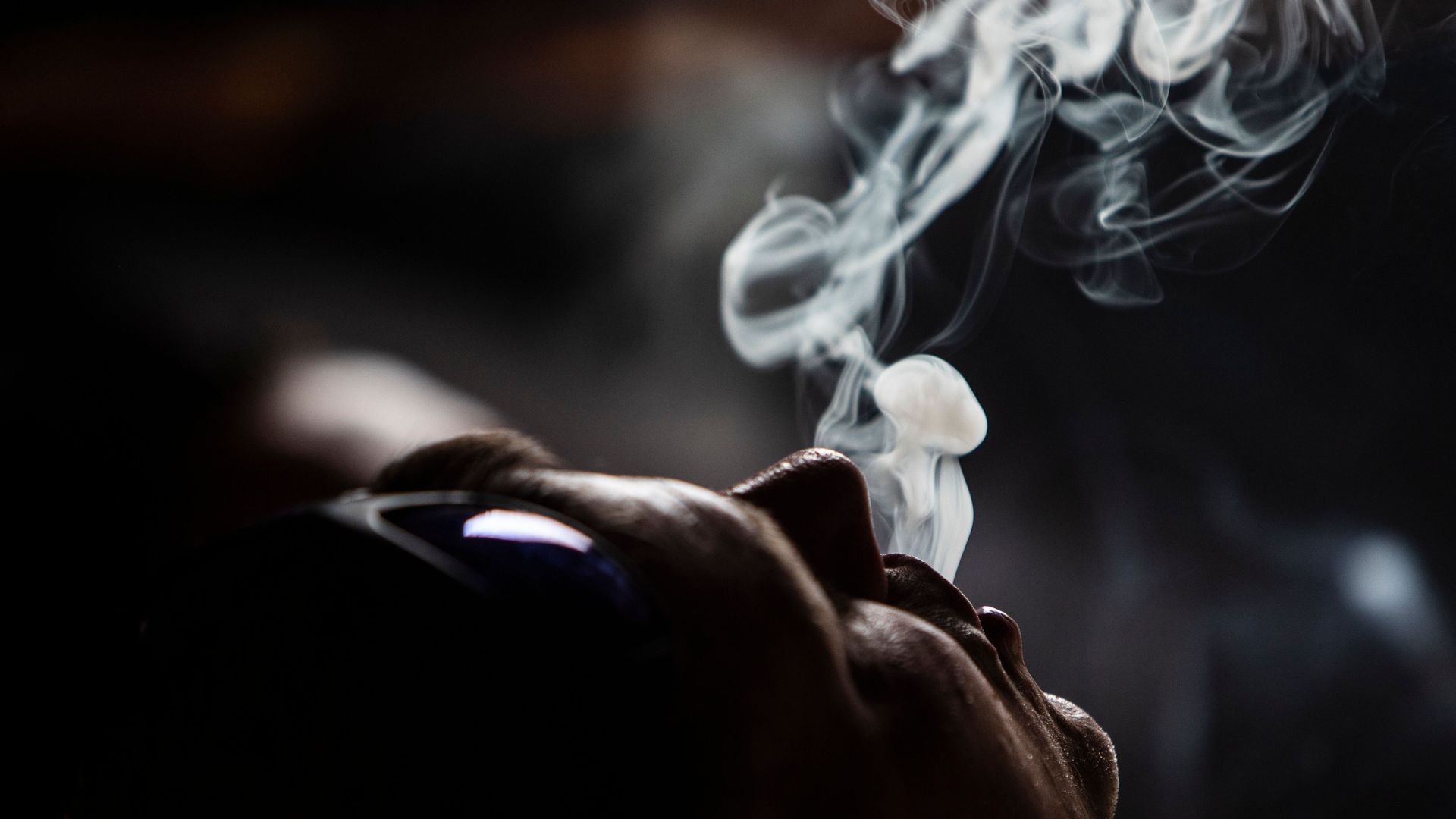 A man leisurely exhales a plume of smoke.