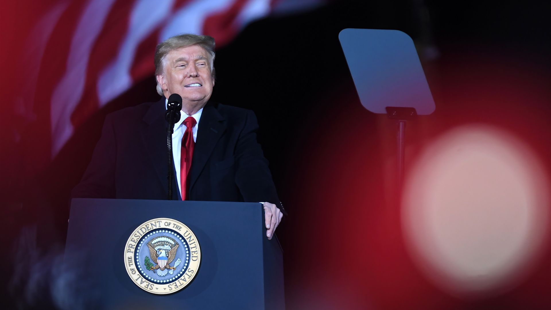 Photo of Donald Trump speaking from behind a podium with the image of the American flag in the backdrop