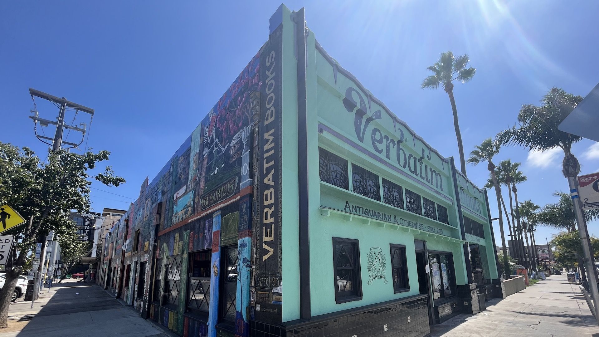Streetview of a bookstore painted with a giant bookshelf mural on one side and bright teal on the other. 