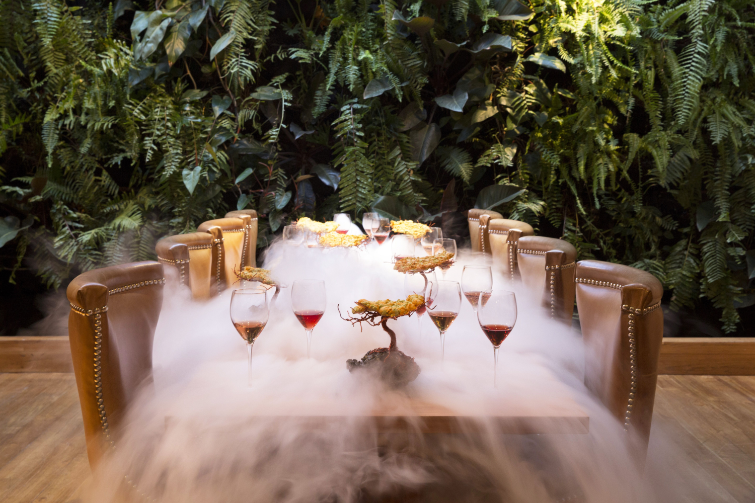 A table set against a backdrop of greenery, smoking with wine glasses 