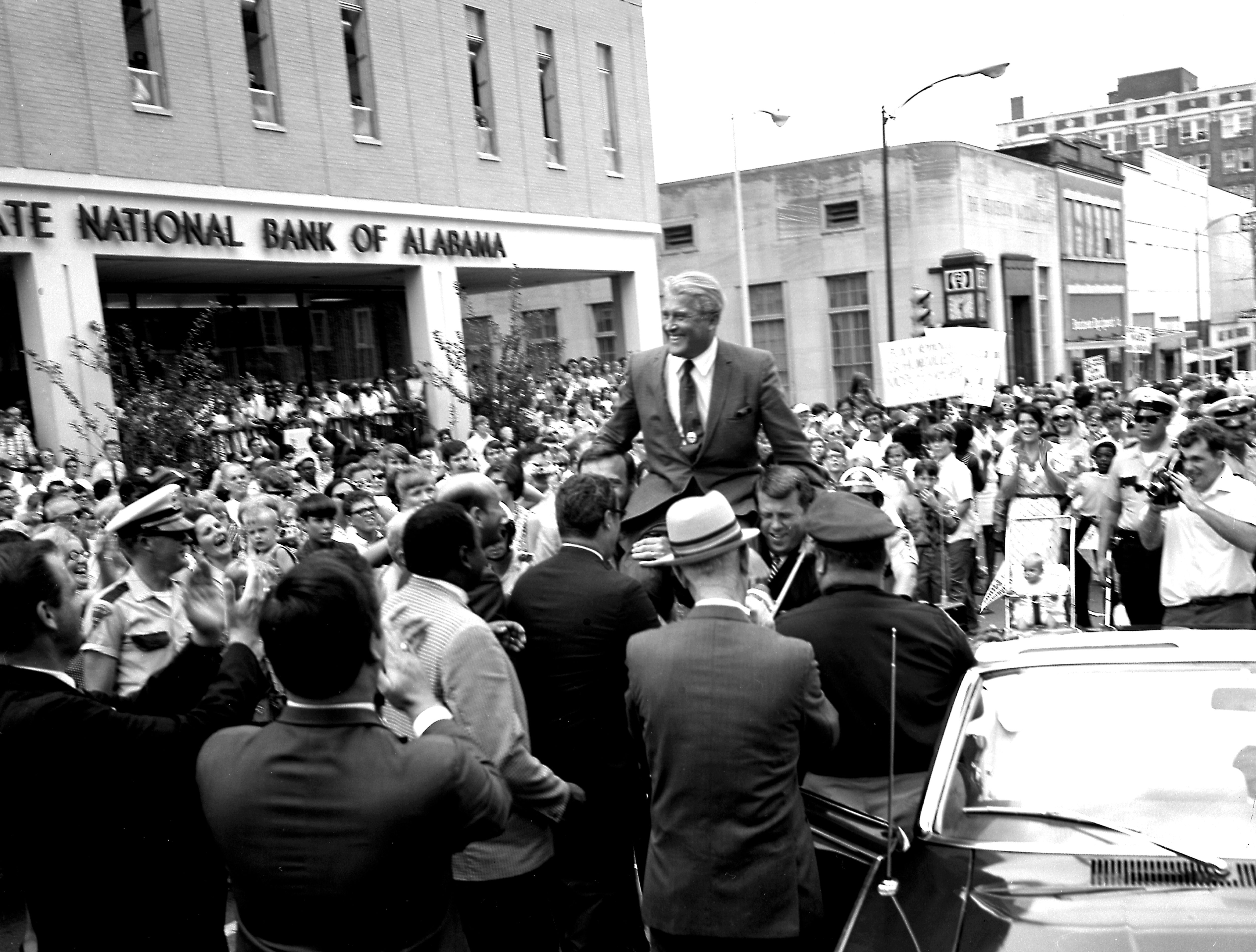 A man, Wernher Von Braun, is lifted on peoples' shoulders amidst a large, celebratory crowd in an black-and-white image from 1969 in downtown Huntsville, Alabama. 