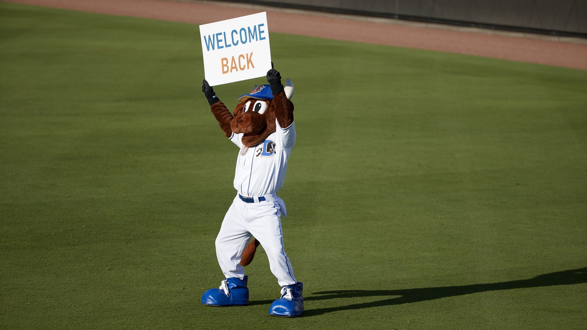 Durham Bulls mascot Wool E. Bull on field holding up sign that reads WELCOME BACK before game at Durham Bulls Athletic Park in 2021.