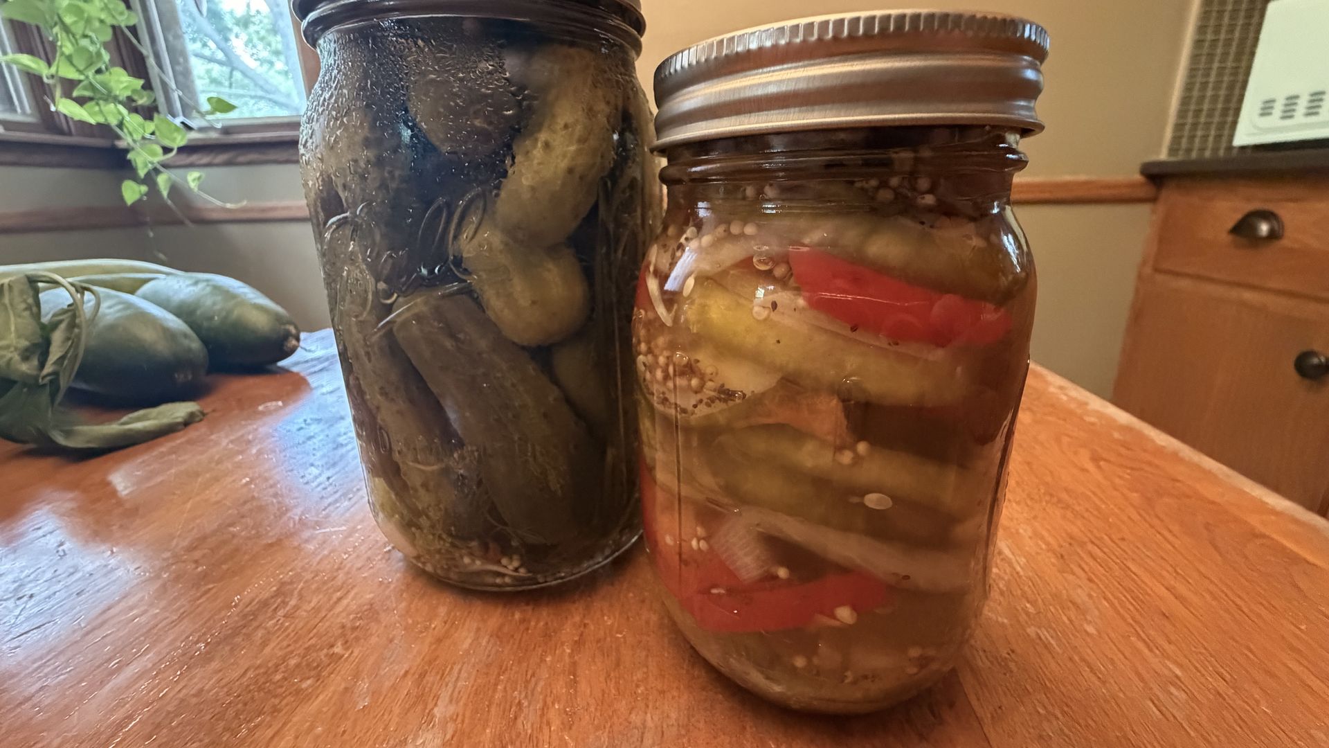 Two jars of pickles sit on a kitchen table.