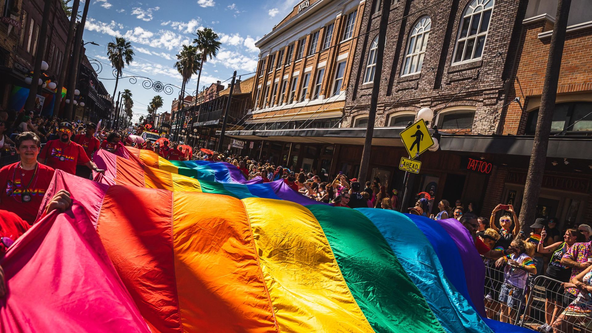 a large rainbow flag being carried during the pride parade in ybor