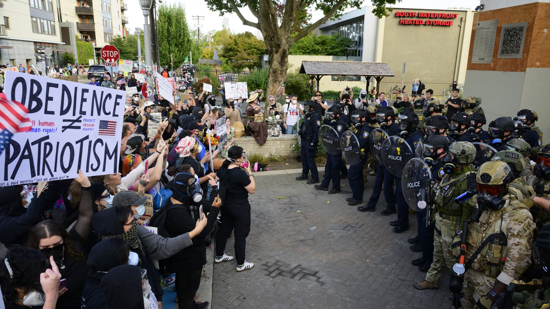 A large protest faces a line of police in riot gear and military-style uniforms outside an ICE facility in South Portland. Protesters hold signs and some wear masks.