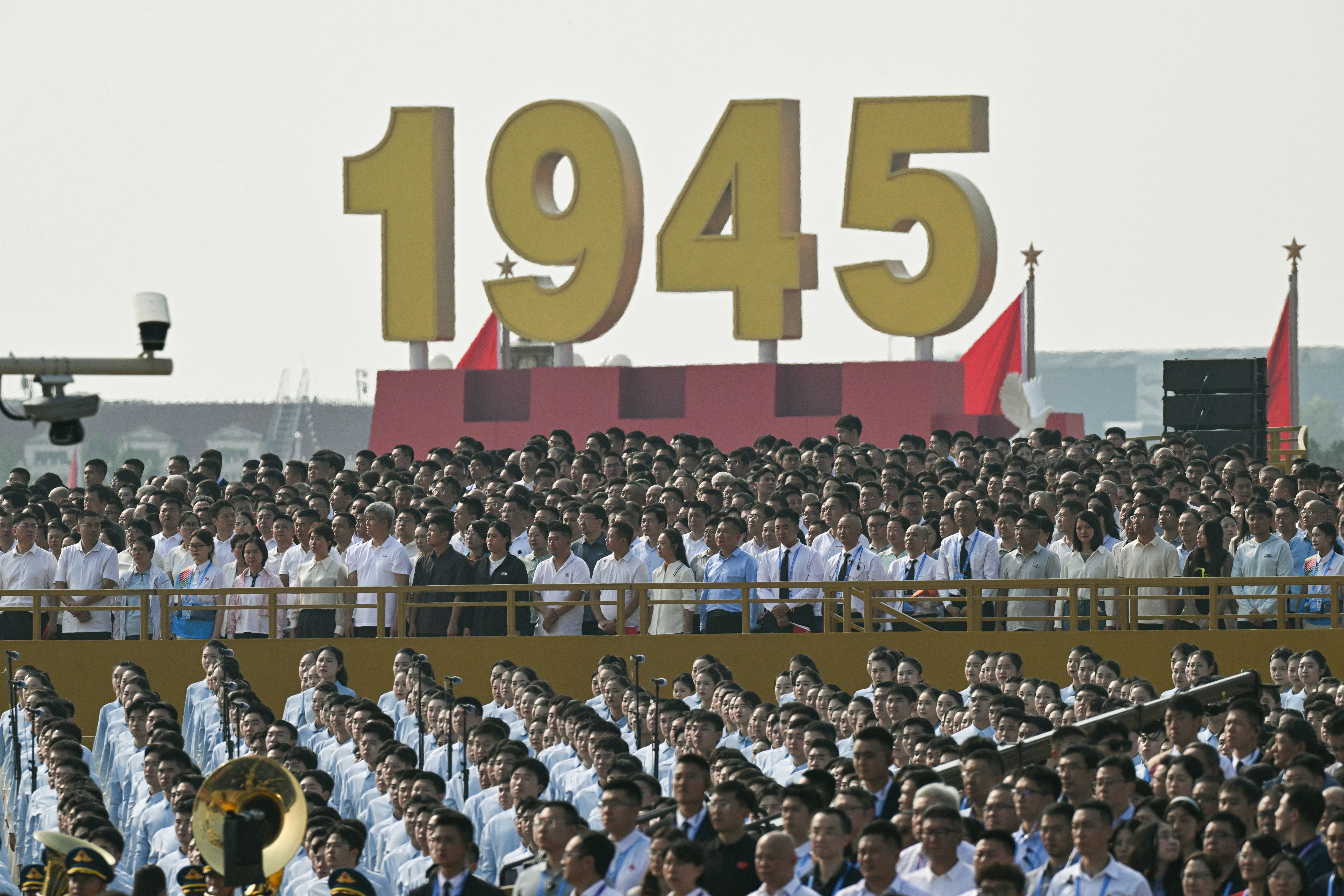 Attendees are seen in the stands at the start of a military parade below a large yellow "1945" sign on a red stand in Beijing's Tiannamen Square.
