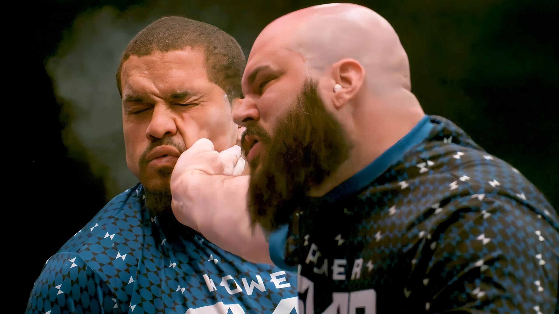 A bald, bearded man slaps another man across the face.