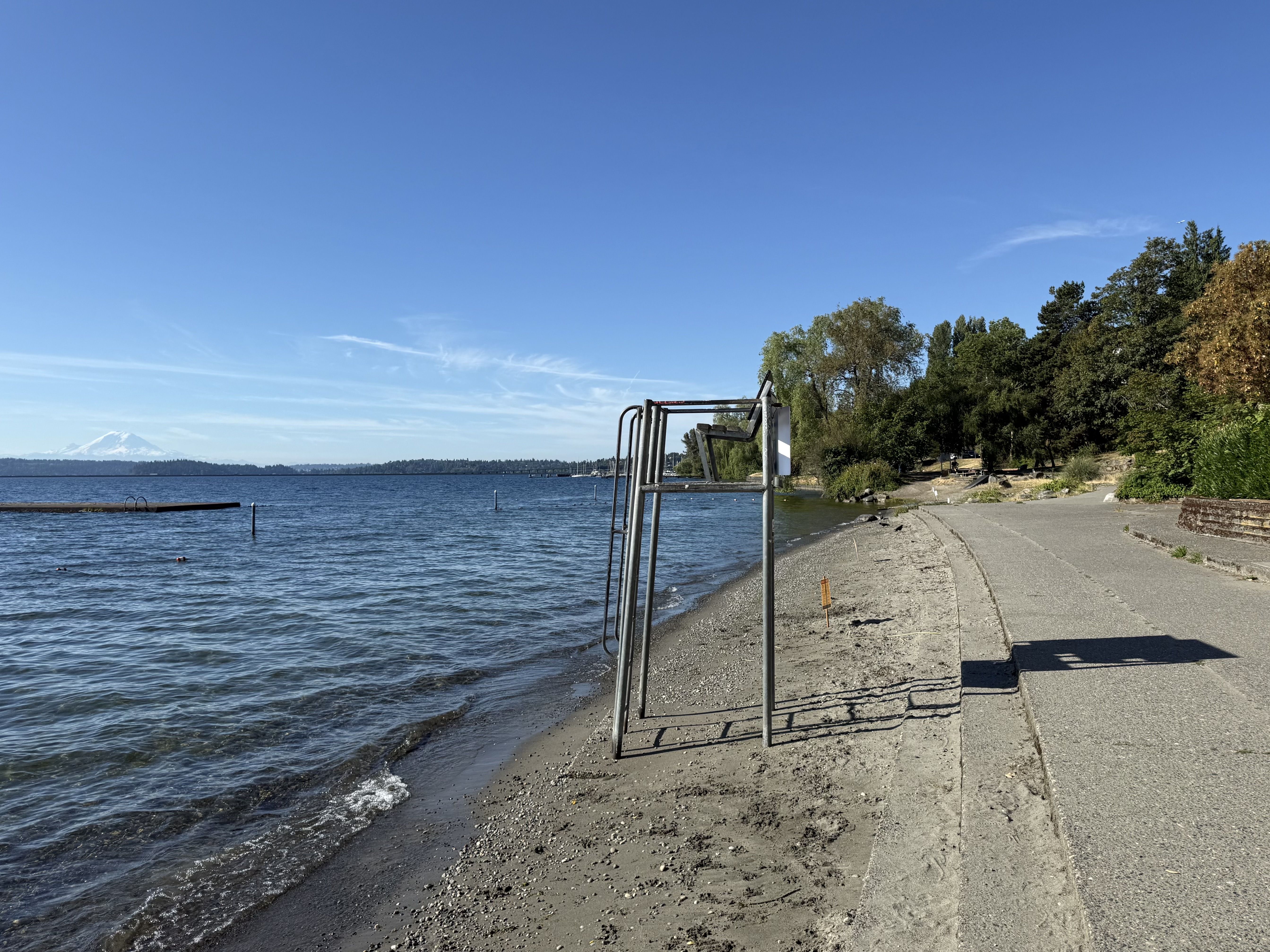 An empty lifeguard stand and trees along Madrona Beach, with Mount Rainier faintly visible in the distance over the water.