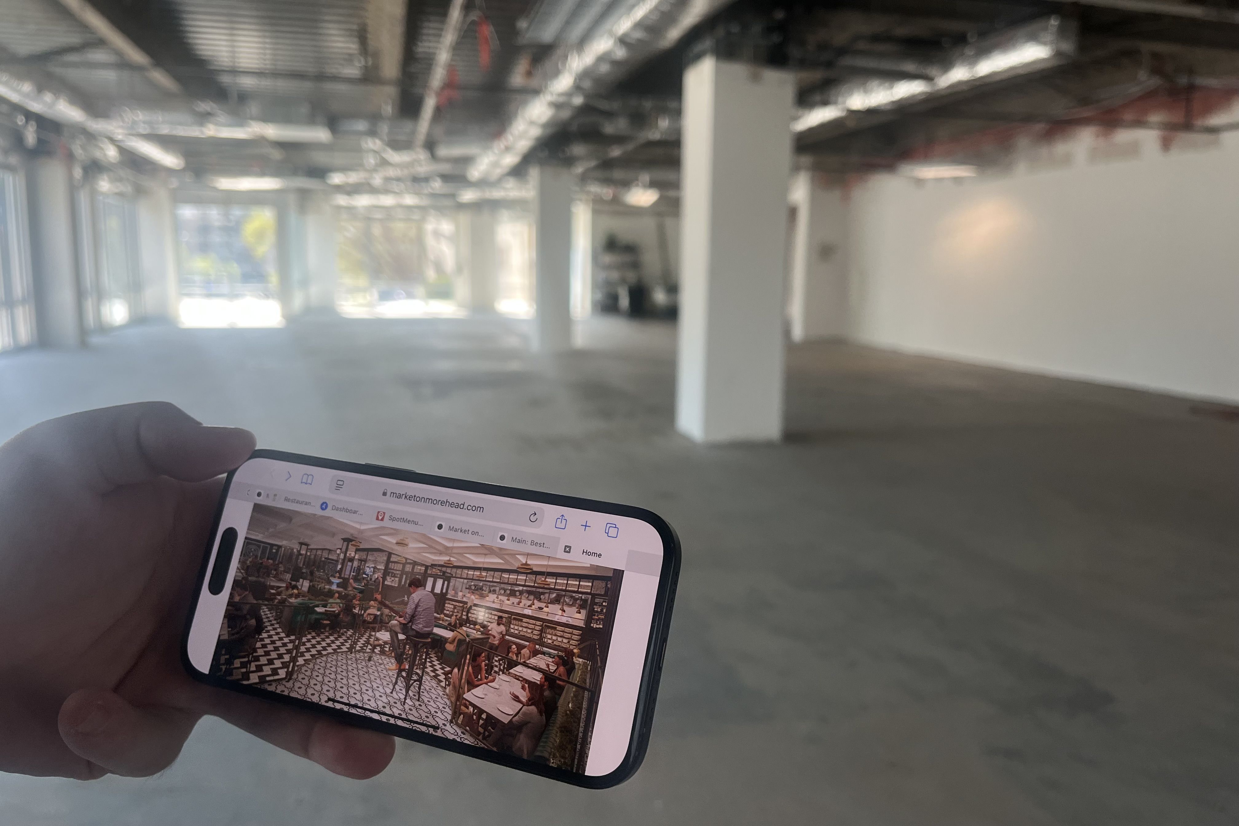 A hand holds a phone with a picture of a rendering in front of an empty room