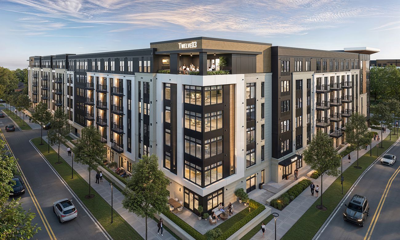 Modern multi-story apartment building with a corner tower, white and dark gray facade, balconies, and a rooftop terrace marked TWELVE03. Tree-lined streets, pedestrians, and parked cars nearby.