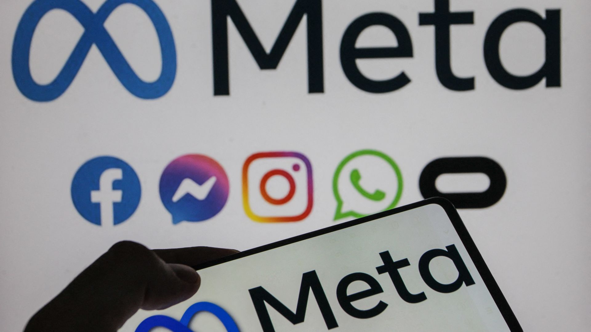 Close-up of the blue Meta infinity logo and the word Meta in black, with colorful social icons (Facebook, Messenger, Instagram, WhatsApp) beneath; a hand holds a card in the foreground.