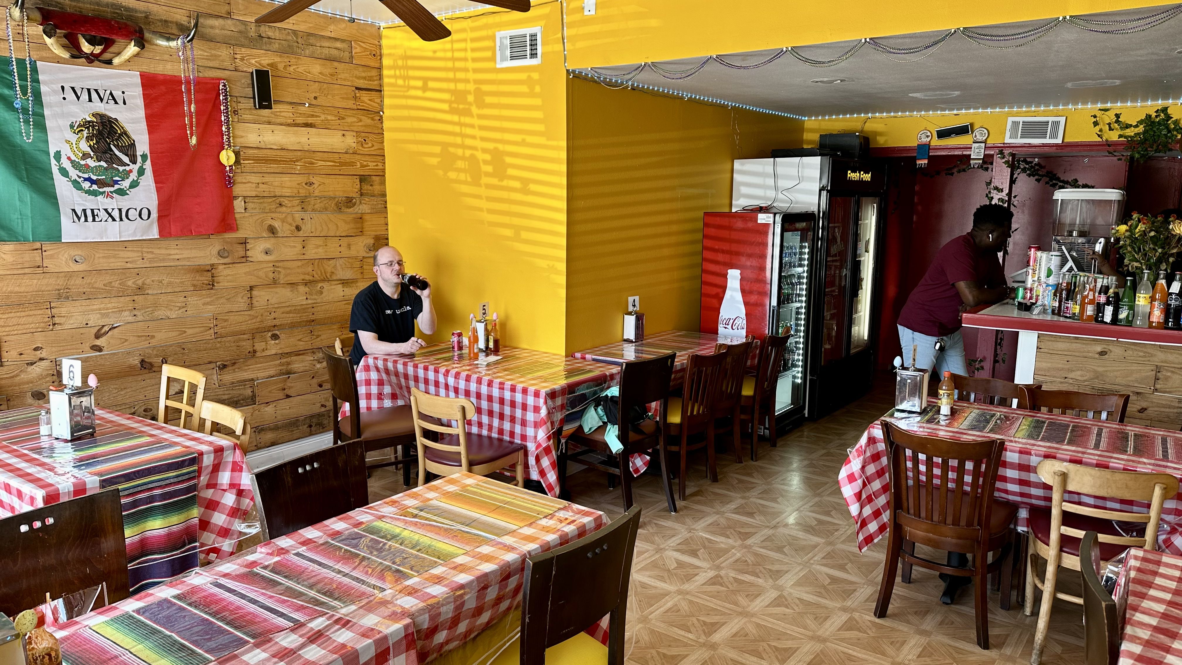 Photo shows the interior of El Rincon with tables and a Mexican flag.