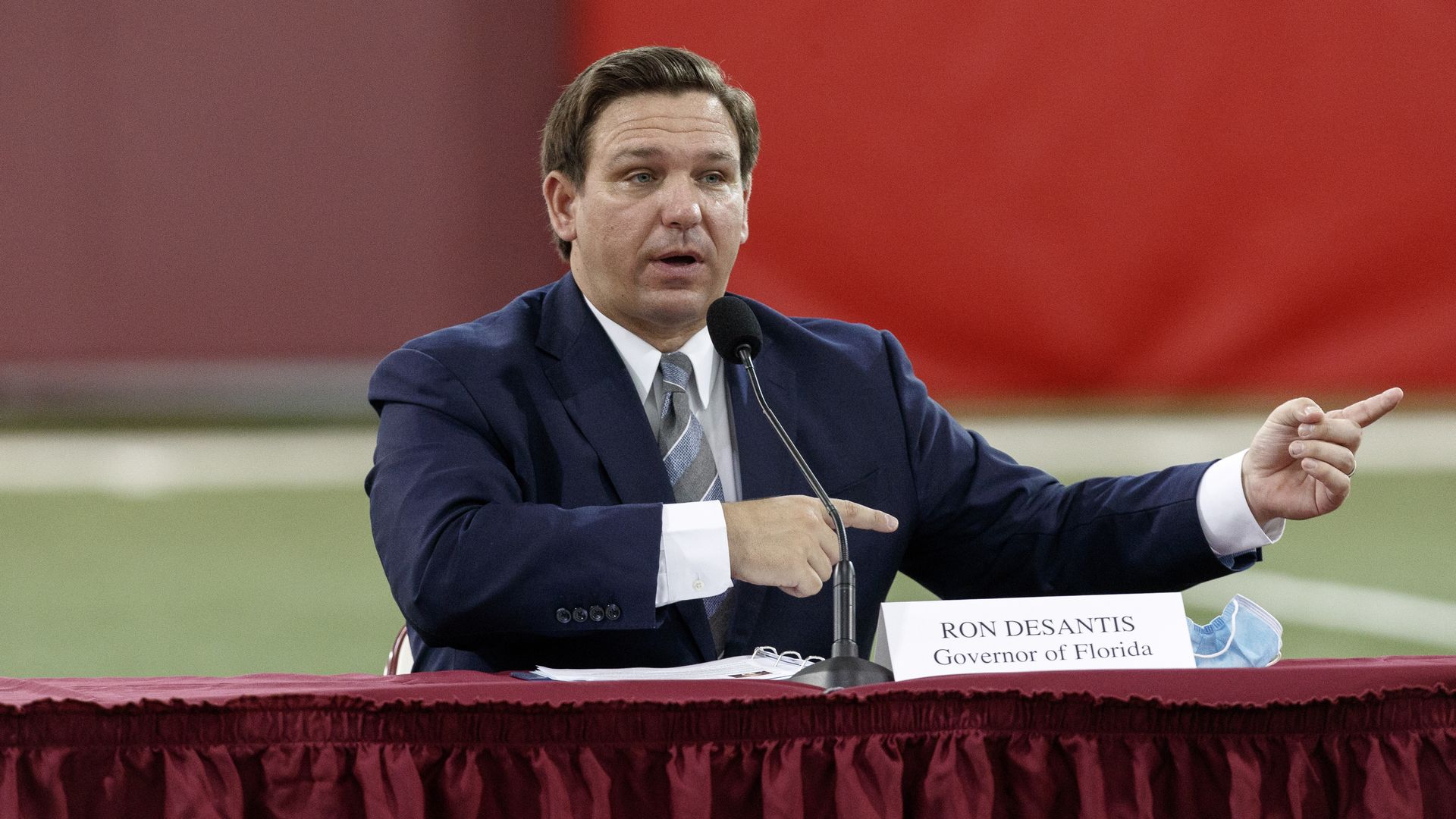 Ron DeSantis sits in front of a microphone, wearing a suit