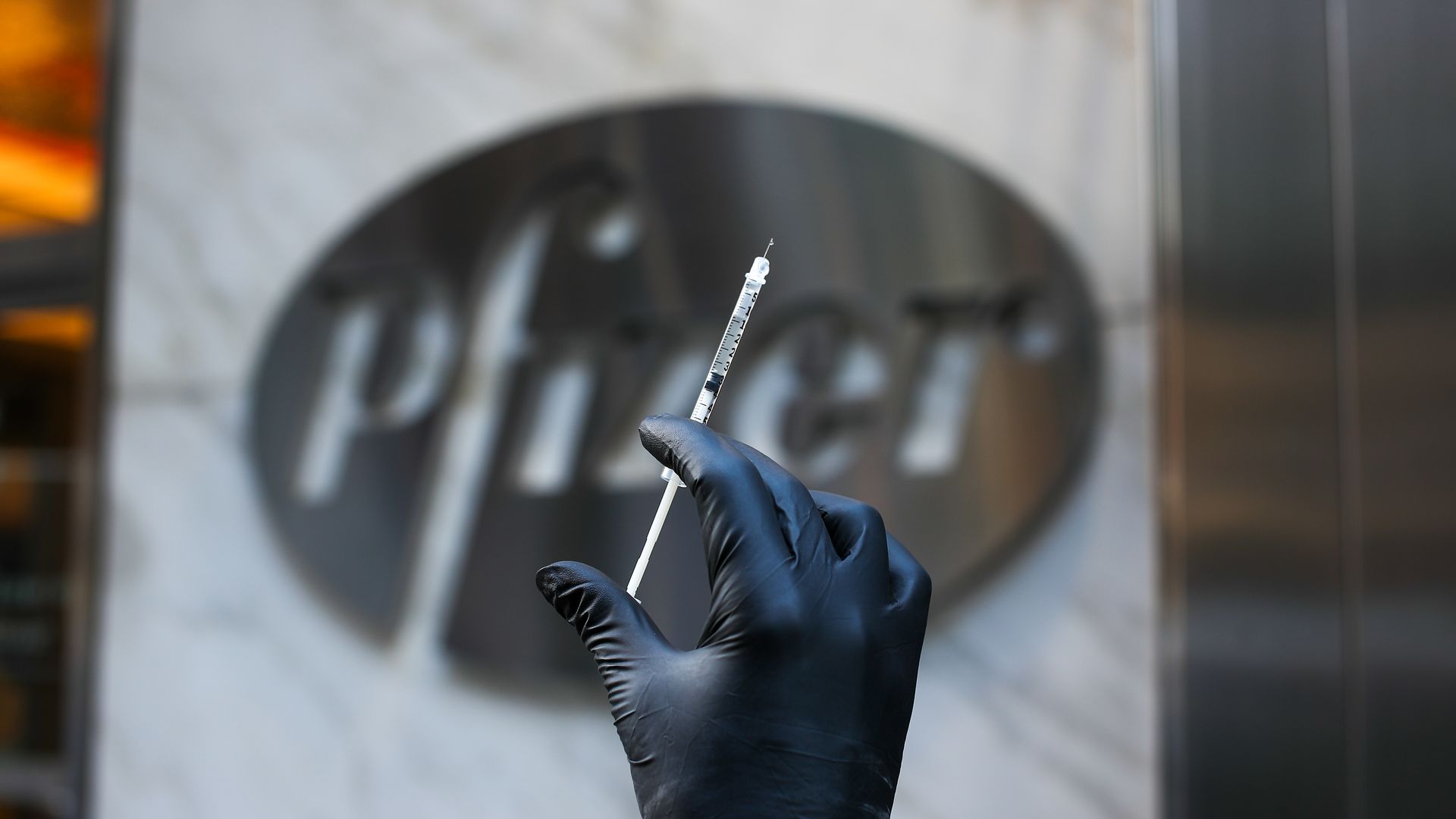 A hand holding a syringe in front of a Pfizer logo