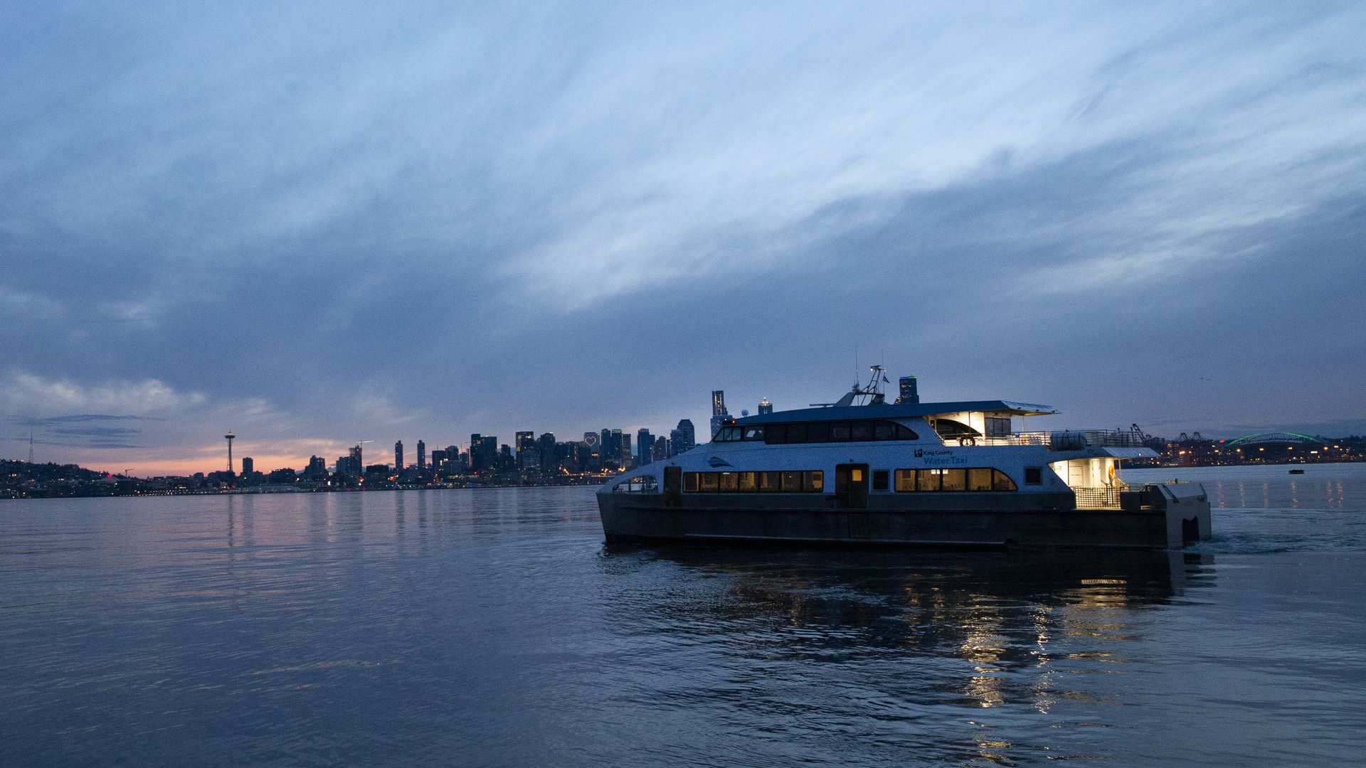 A water taxi plies the waters with the Seattle downtown skyline in the background as sunset falls.