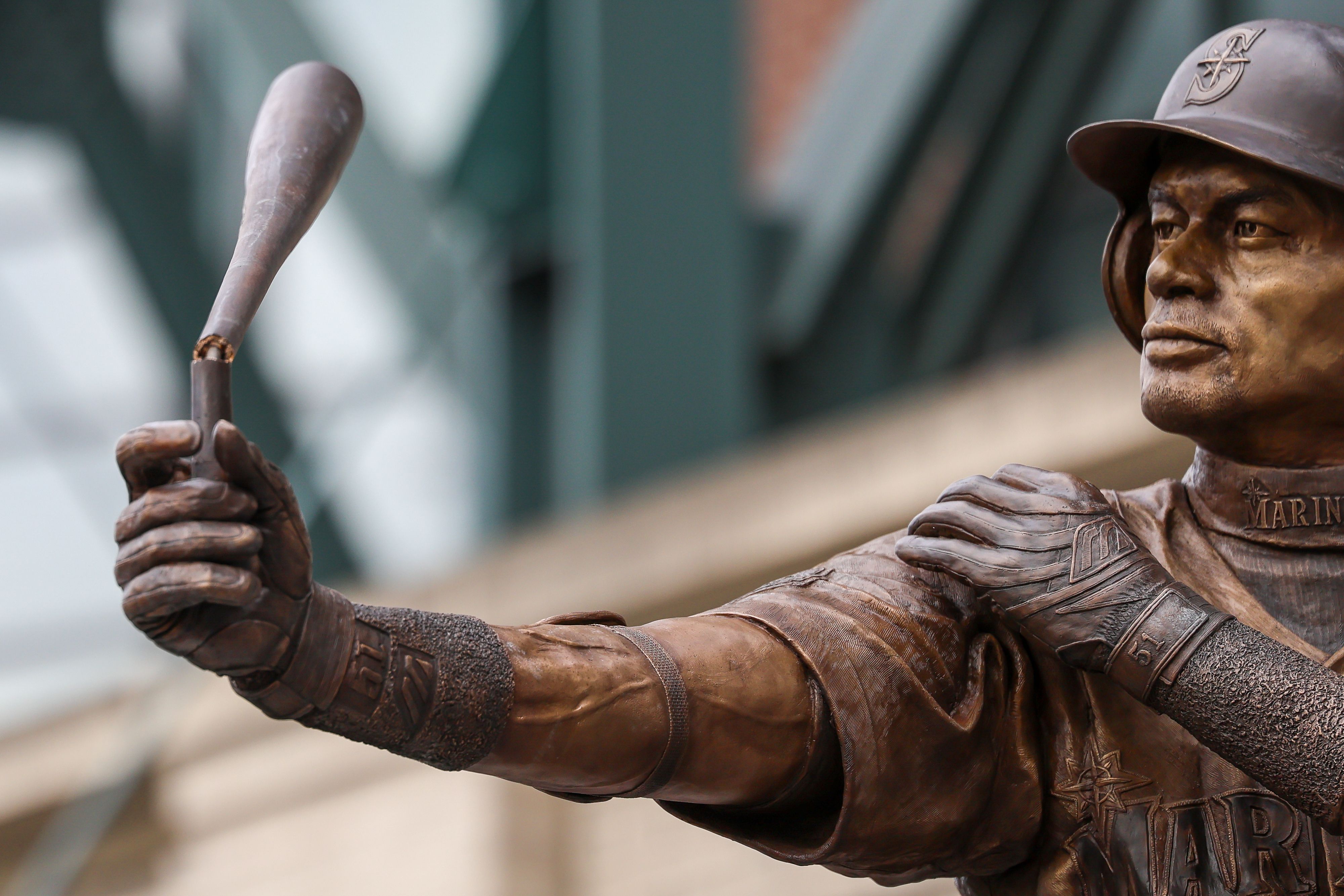 A close up of a metal statue of Ichiro Suzuki holding a bat that is broken backward.