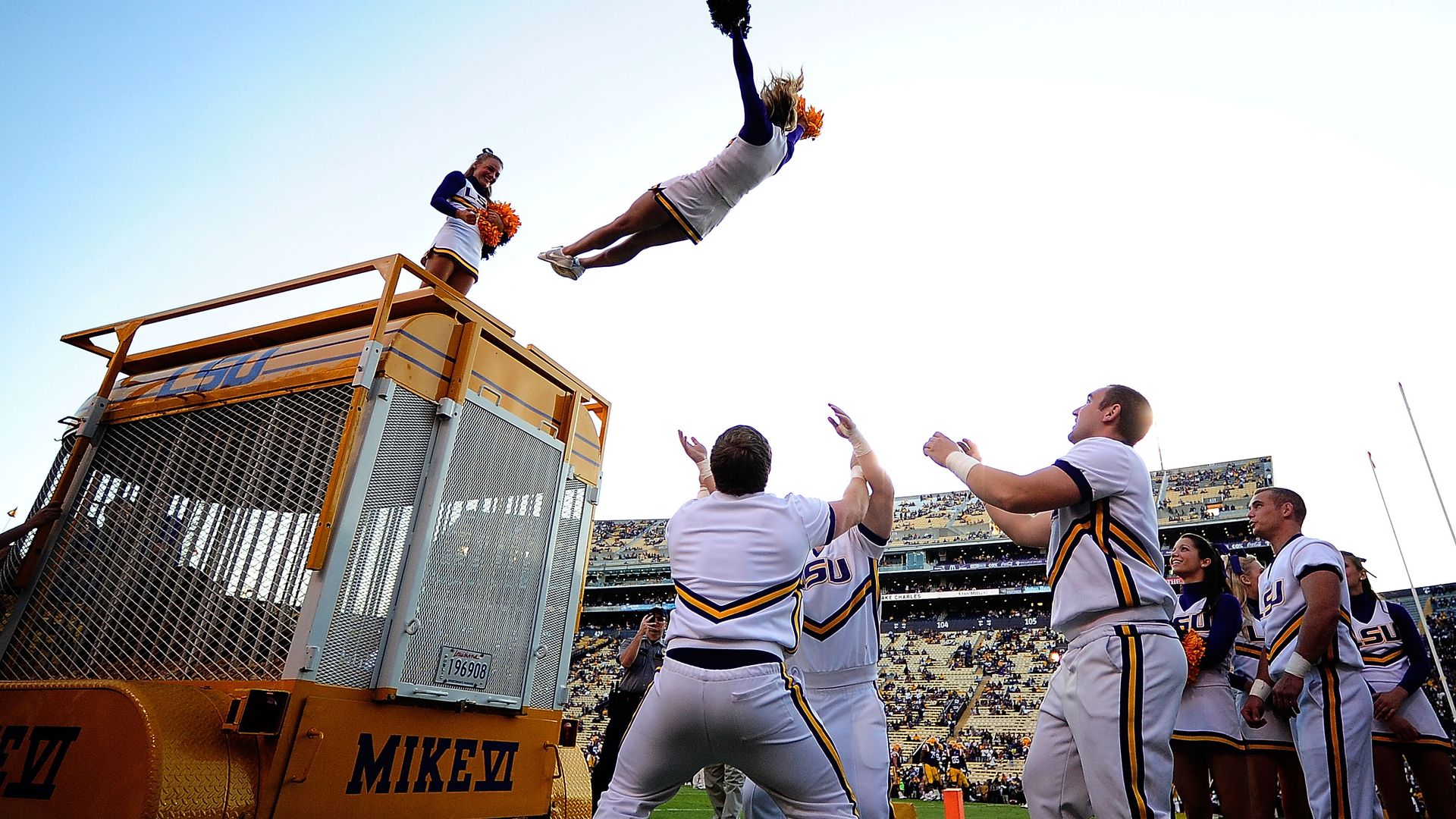 Image shows LSU cheerleaders doing a stunt off Mike the Tiger's enclosure at a football game.