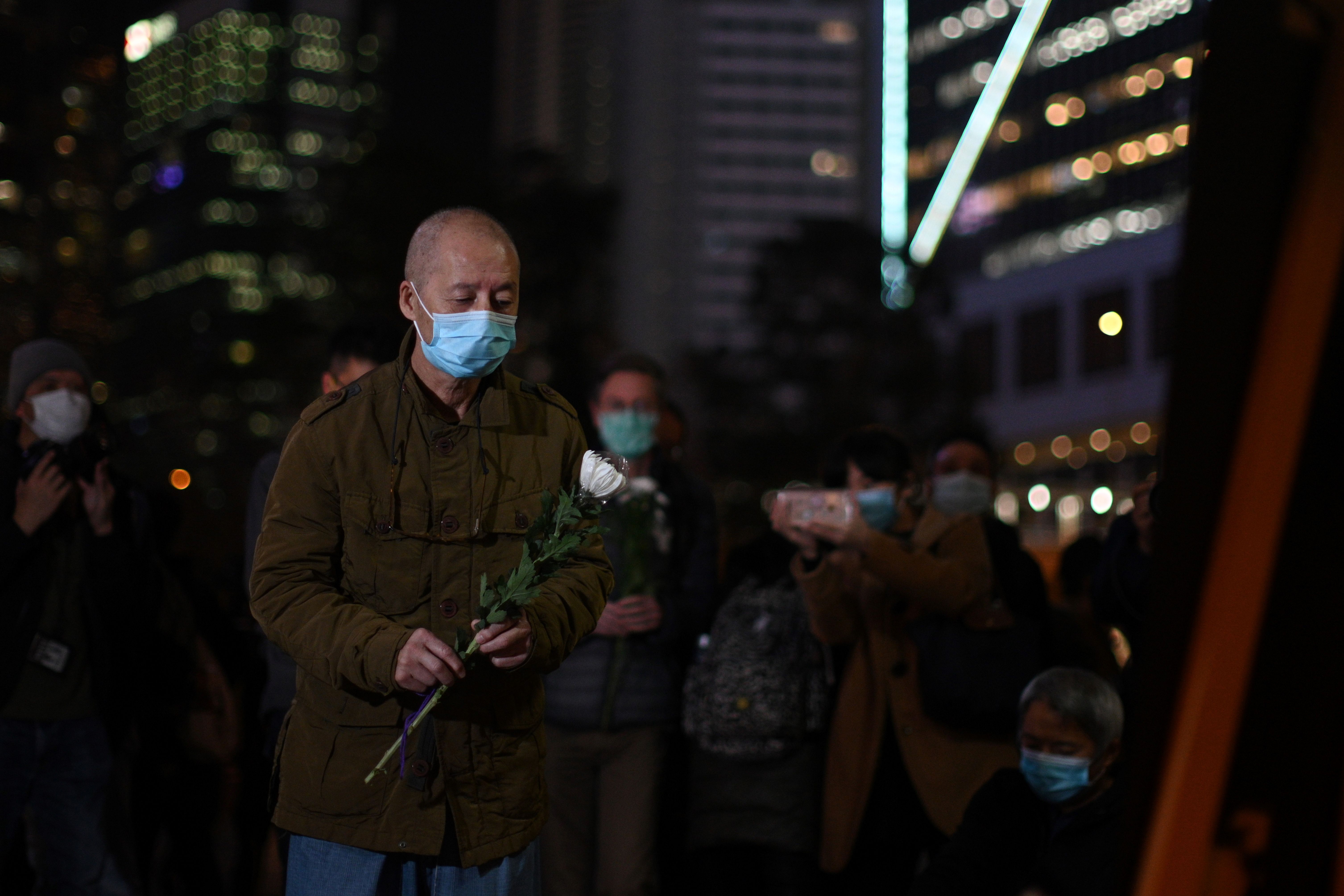 In this image, a man wearing a protective face masks carries a rose at the vigil at night