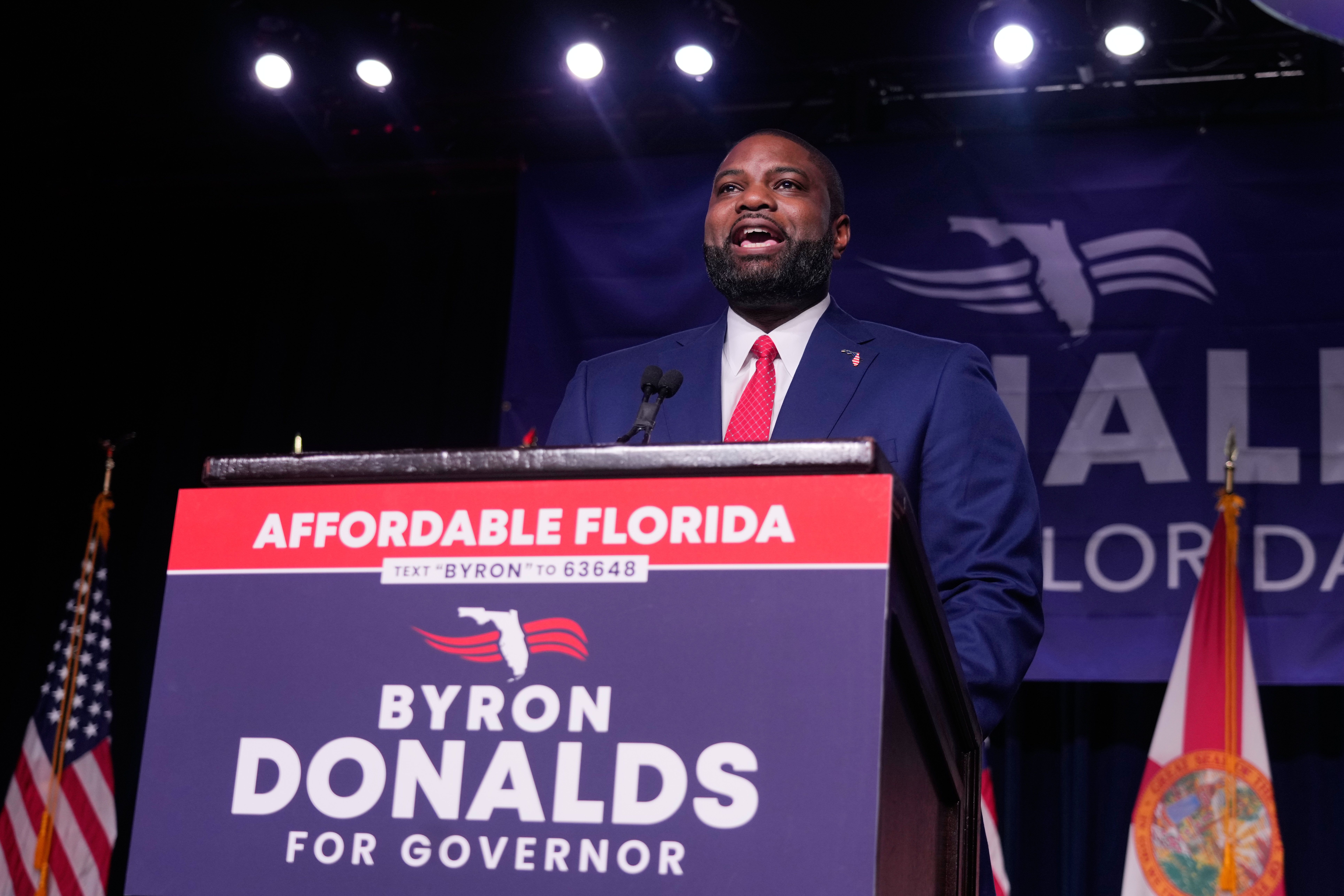 Byron Daniels stands up on stage, behind a podium in this photo, taken from the perspective of an audience member