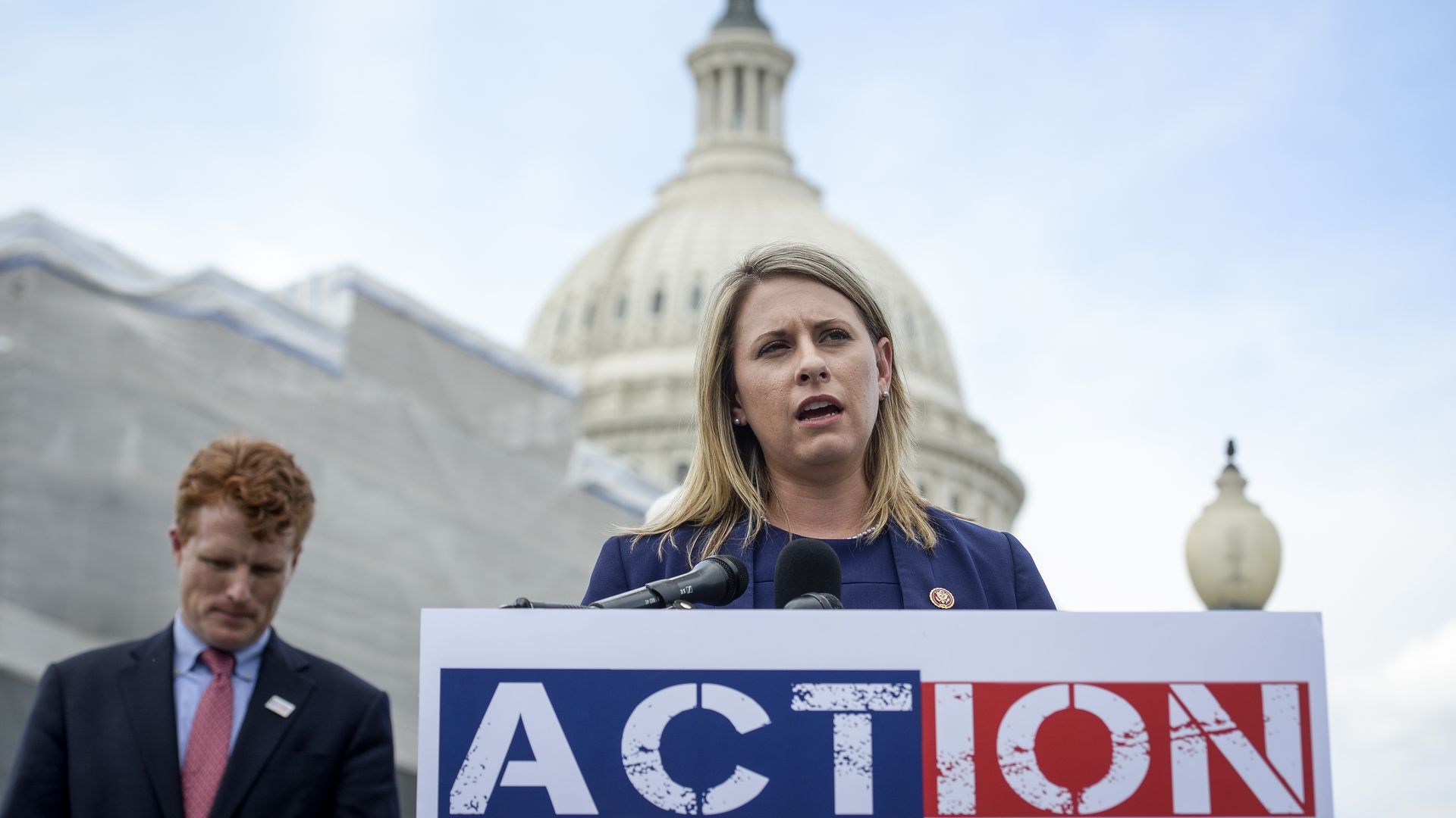 Photo of Katie Hill speaking from behind a podium against the backdrop of the White House
